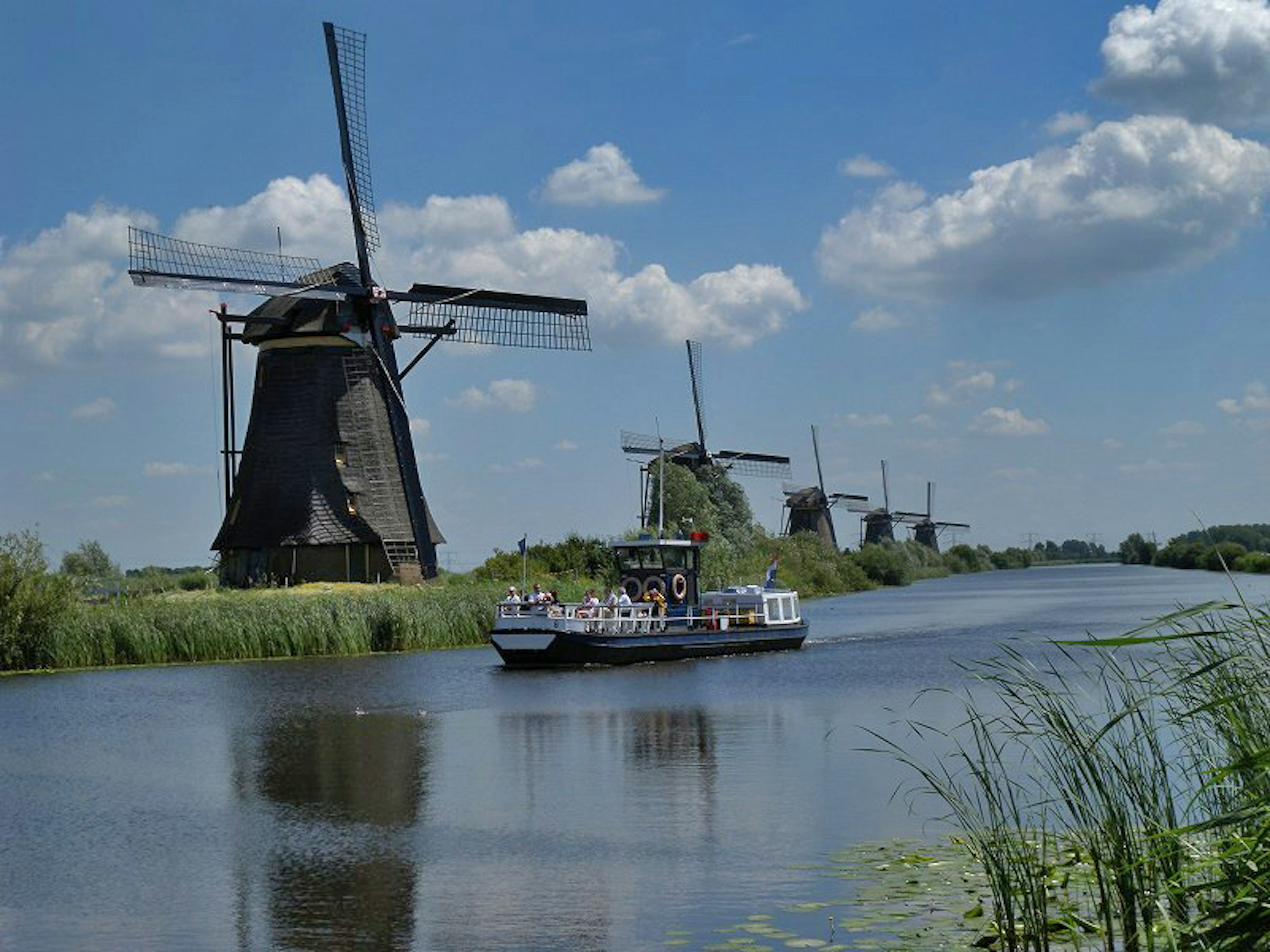 Malersicher Blick mit Windmühlen und einem Boot auf einem ruhigen Fluss