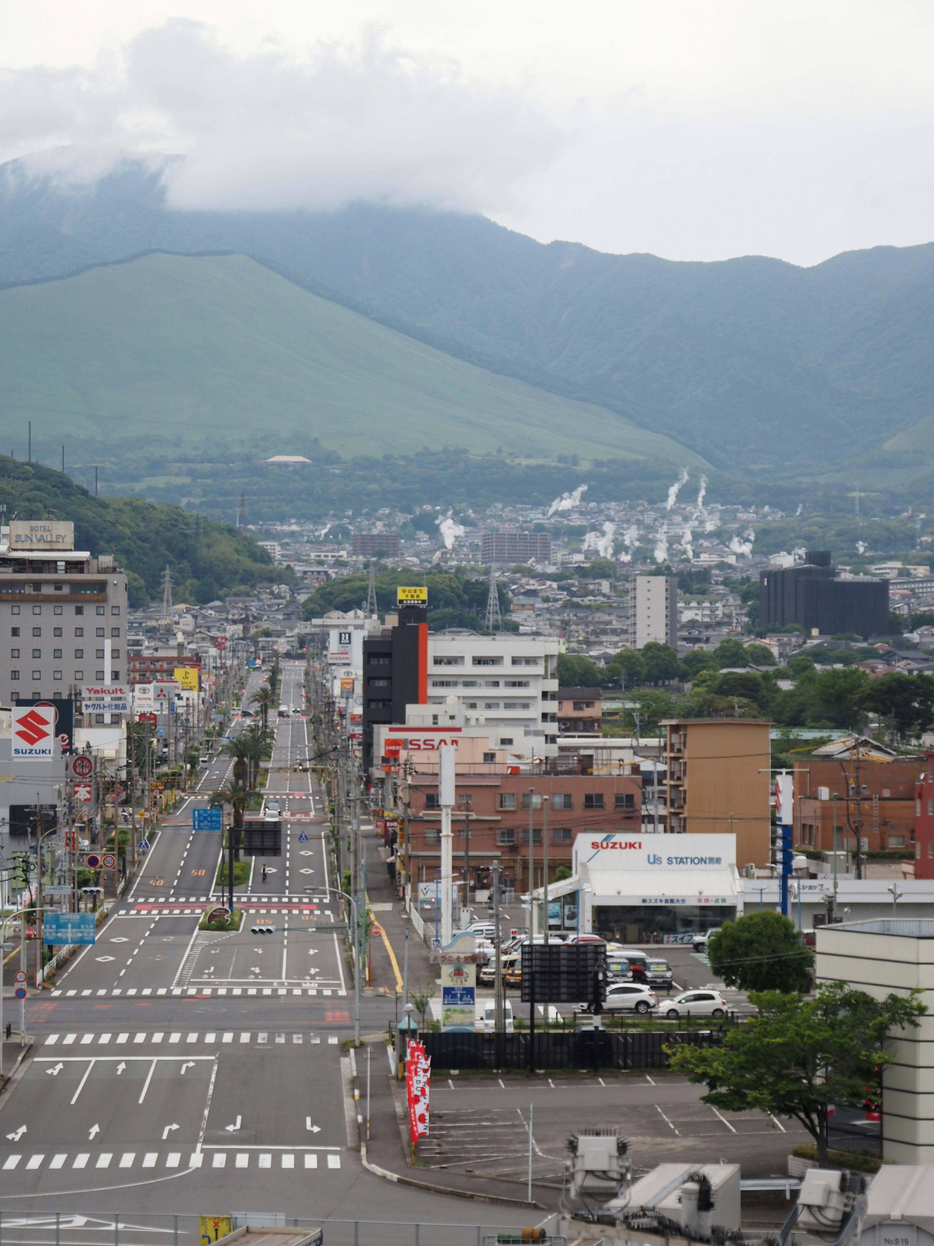 Wide street with a backdrop of green mountains and urban landscape