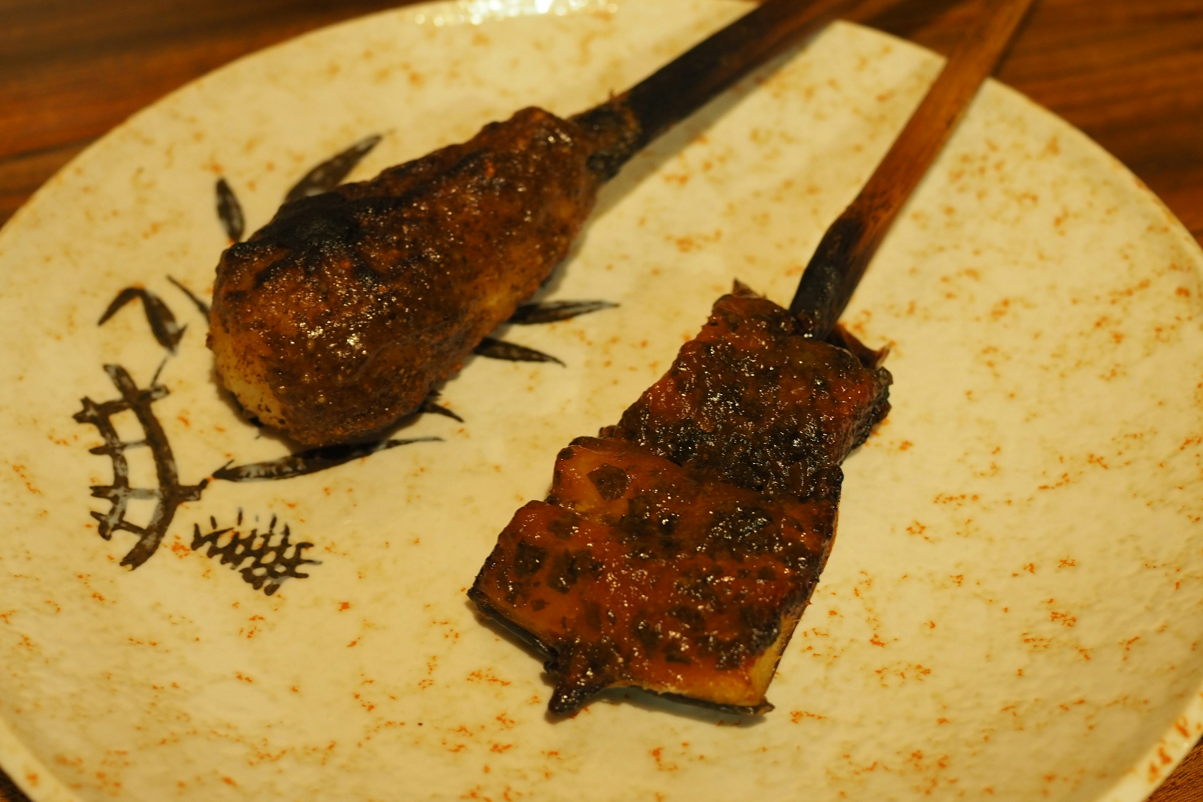 Grilled skewers of chicken and eel with a glossy glaze on a decorative plate