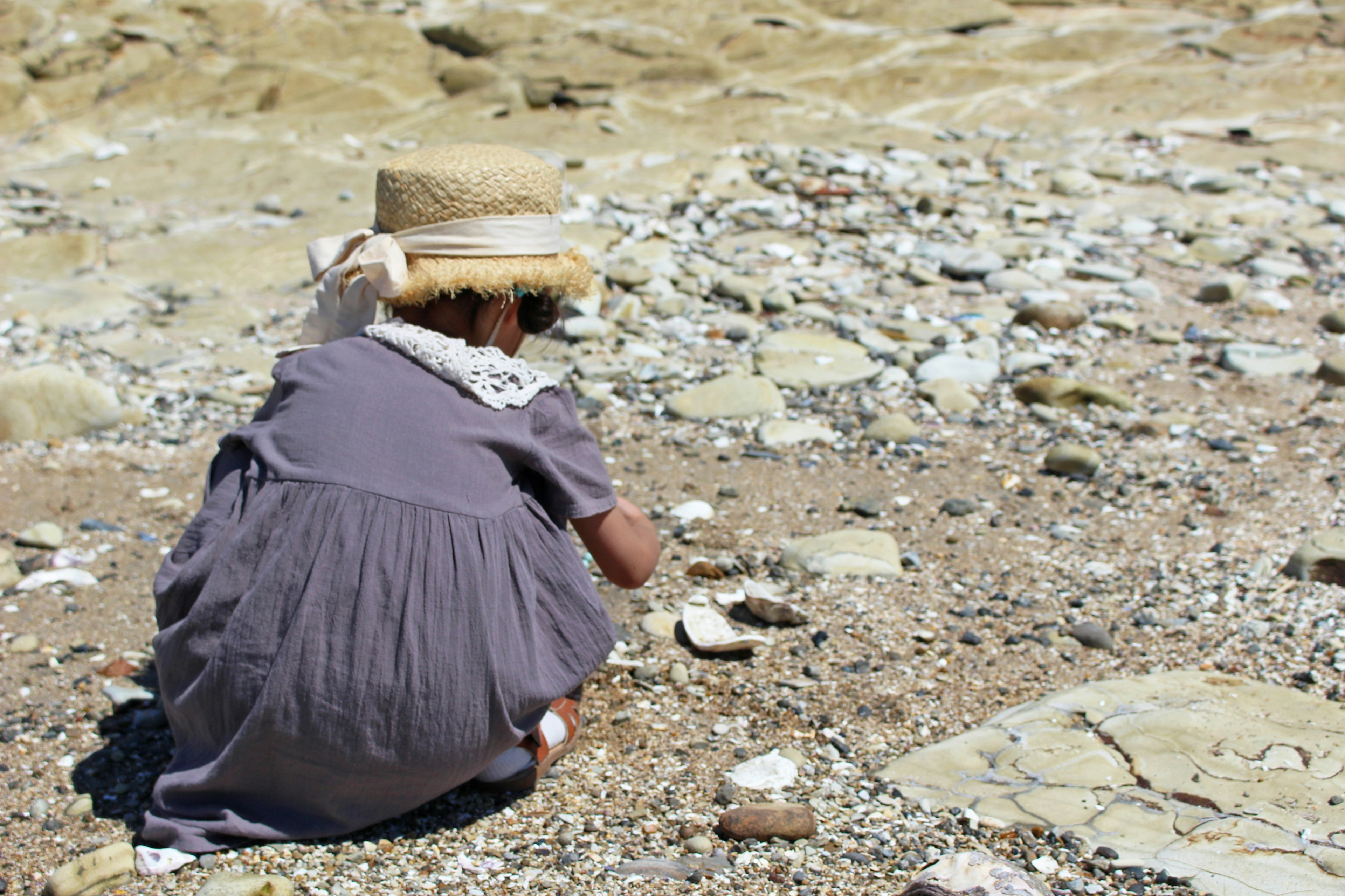 Kind mit Strohhut, das Steine am Strand sammelt