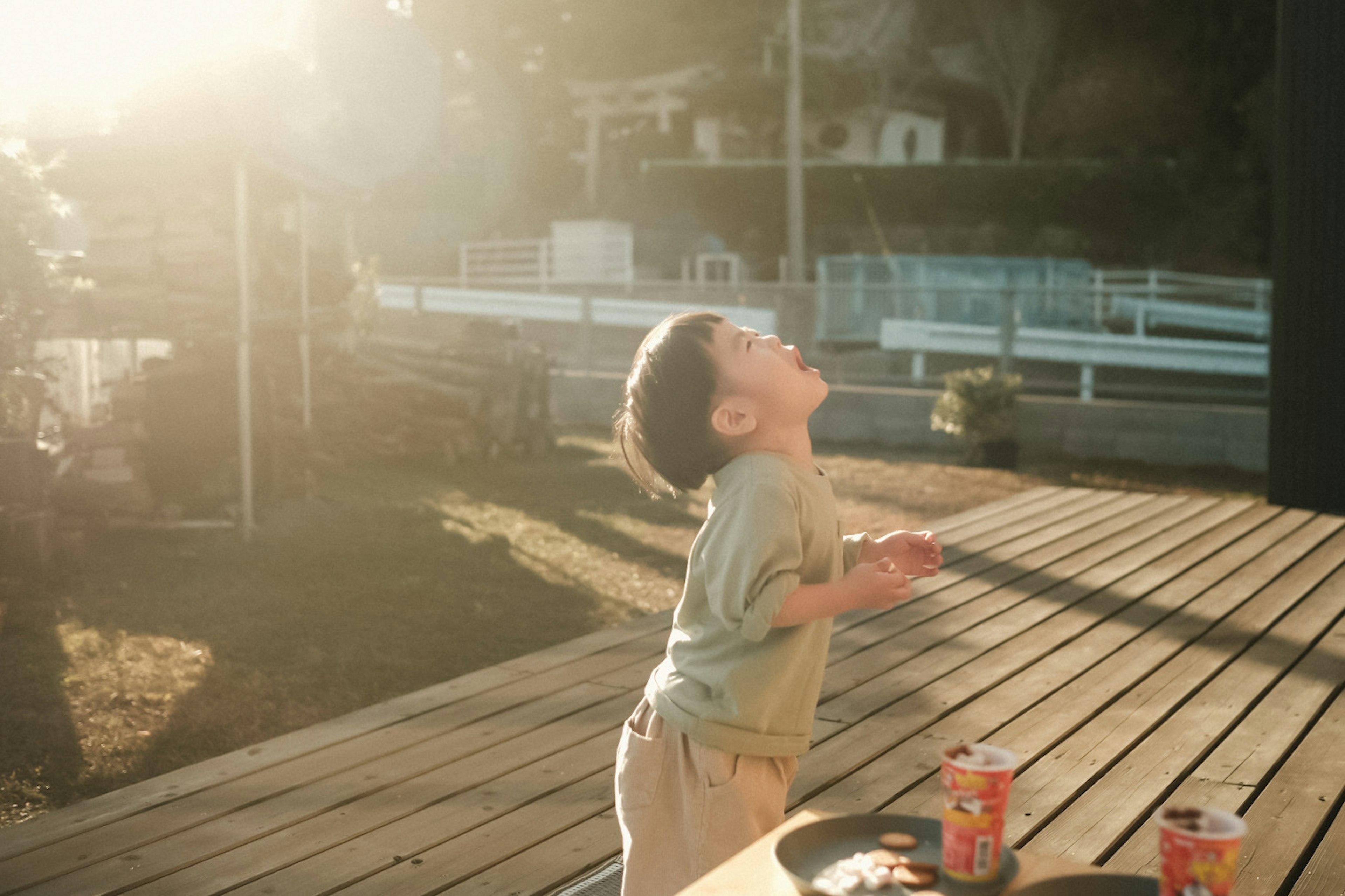 Child looking up at the sky in bright sunlight on a wooden deck