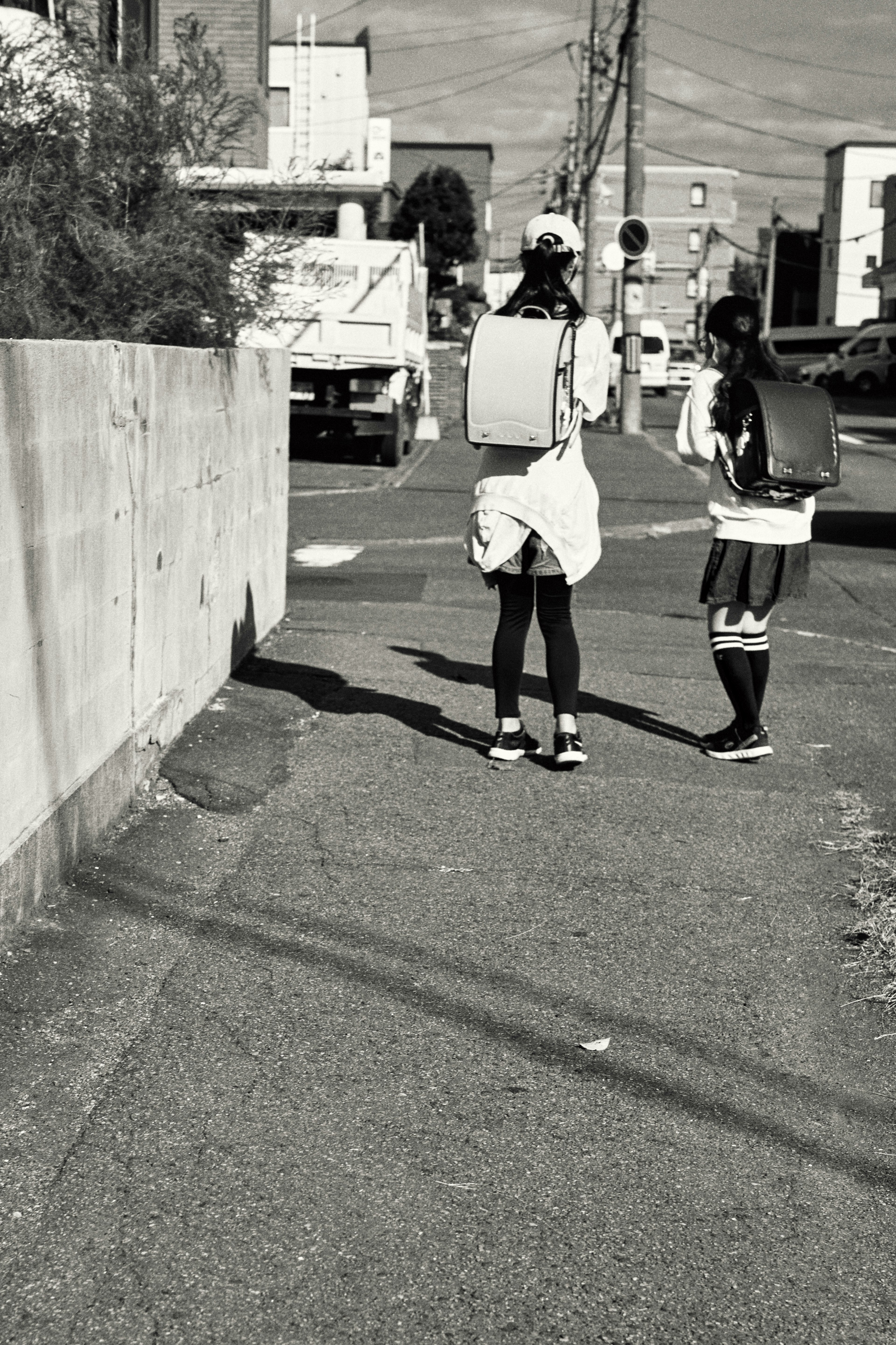 Deux enfants marchant dans une rue avec des sacs à dos en noir et blanc