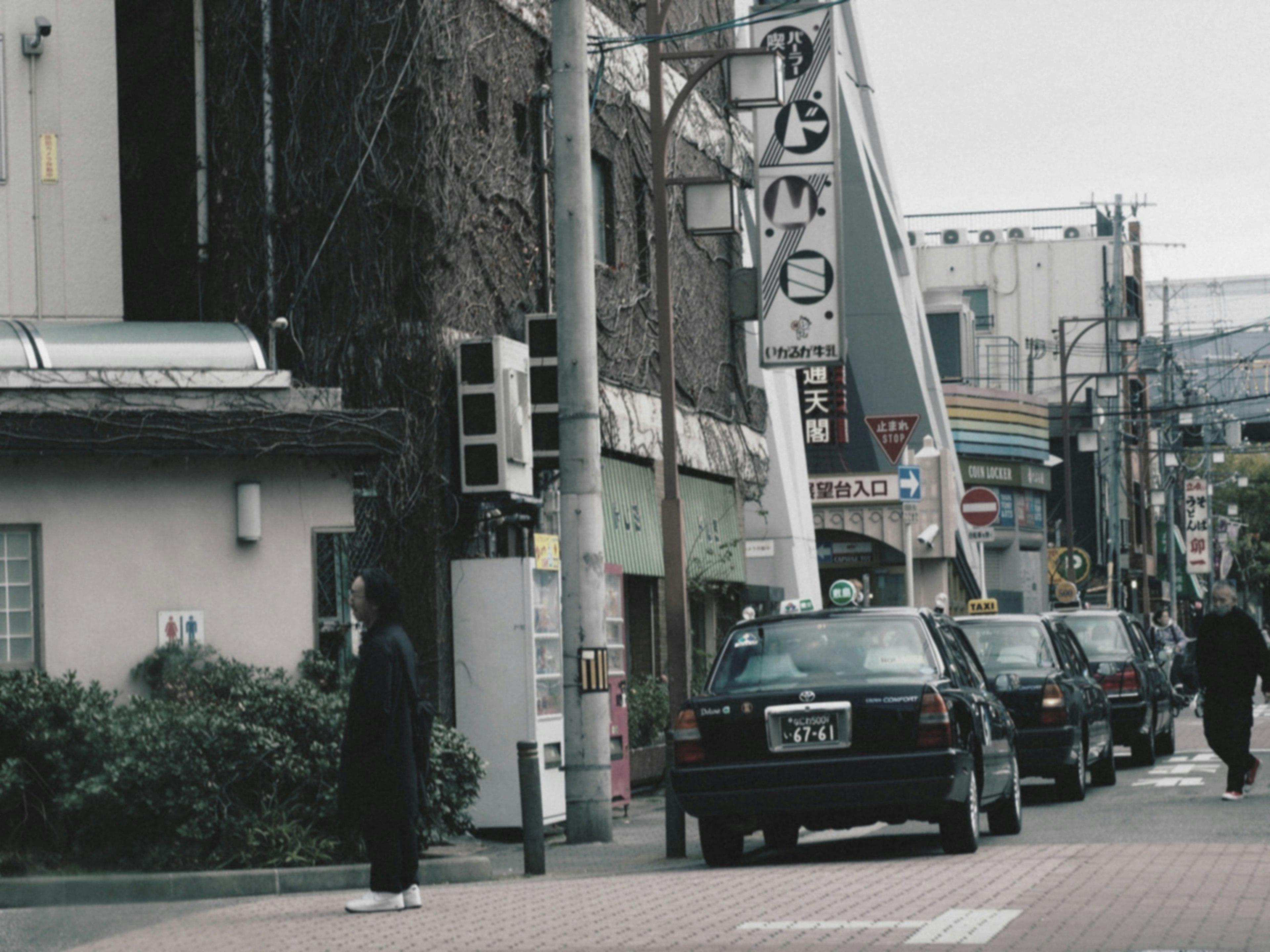 Urban street scene featuring a person standing at the corner and cars parked along the road