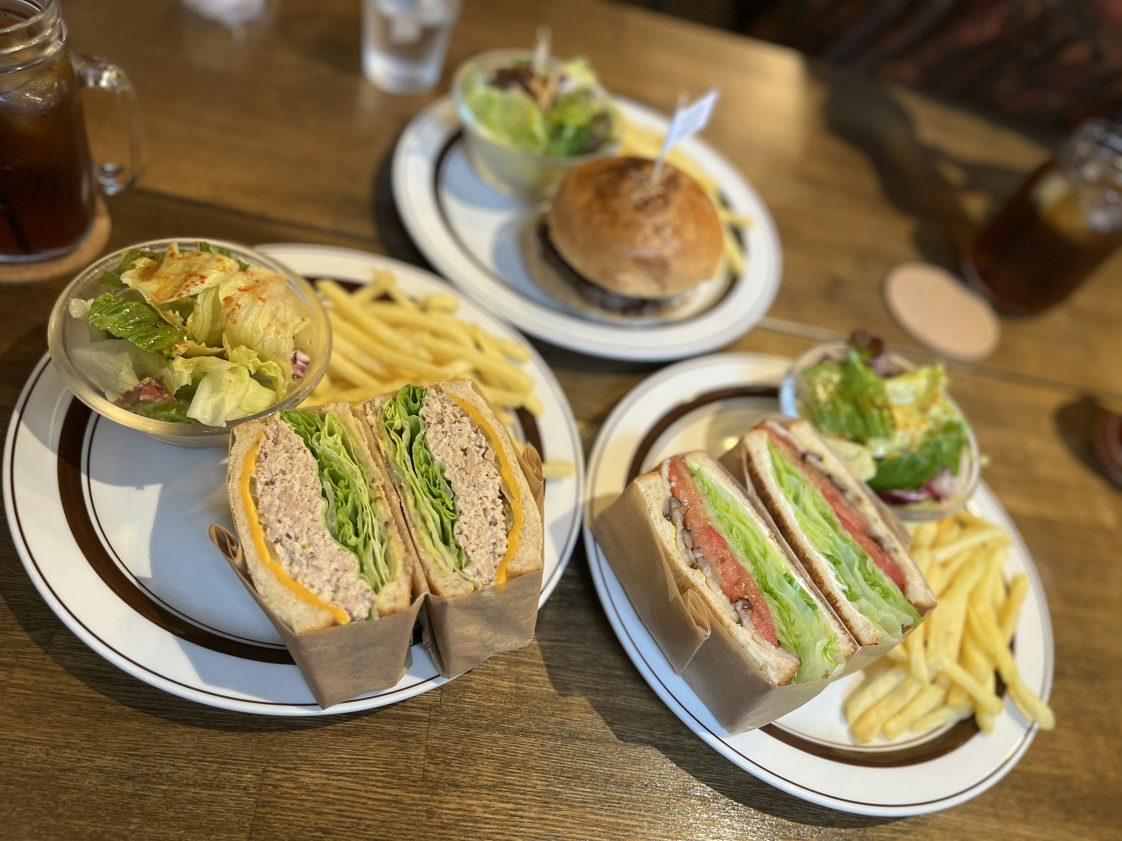 Platos de sándwiches y una hamburguesa con ensalada y papas fritas en una mesa de madera