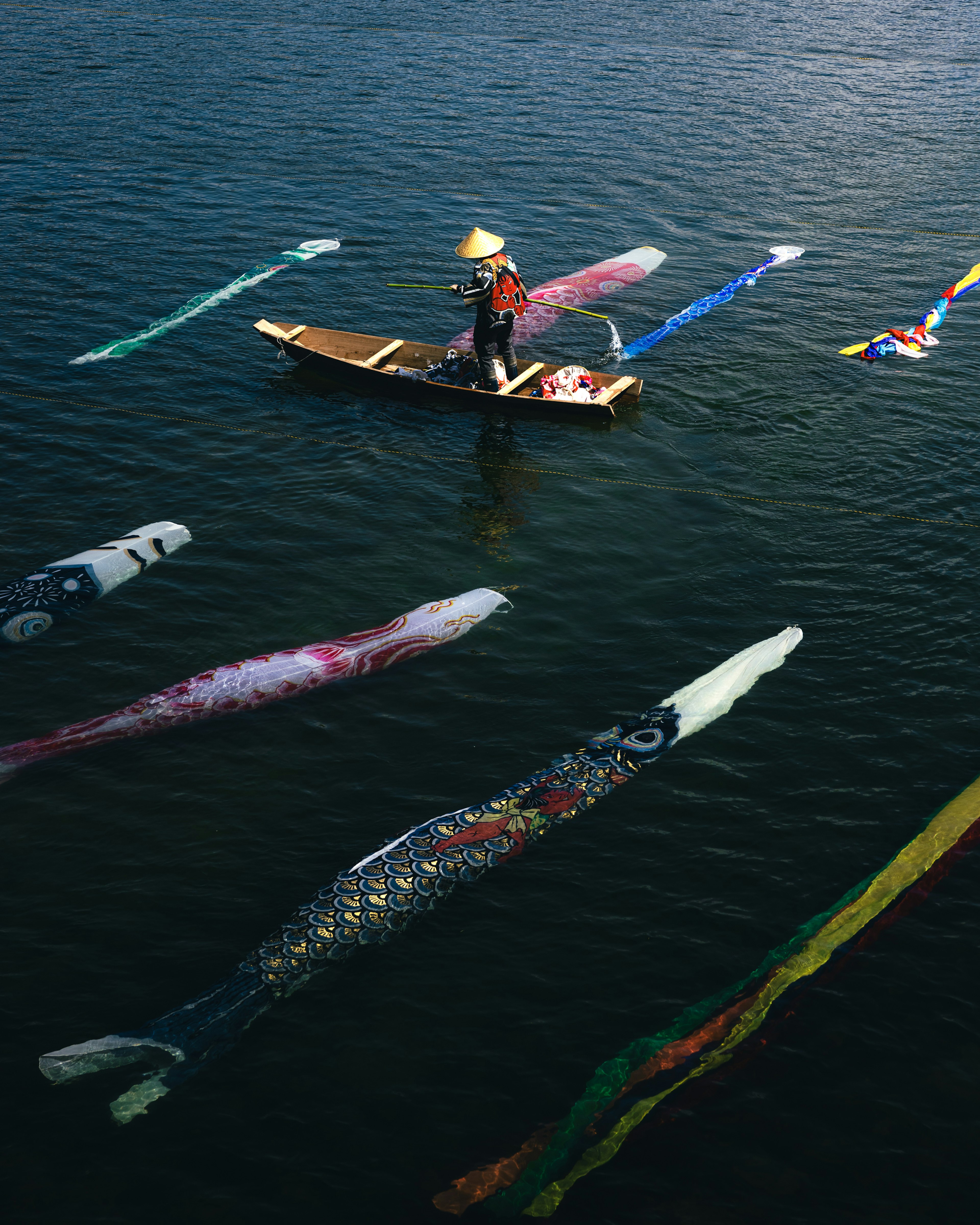 Fisherman in a boat surrounded by colorful decorative fish shapes on the water