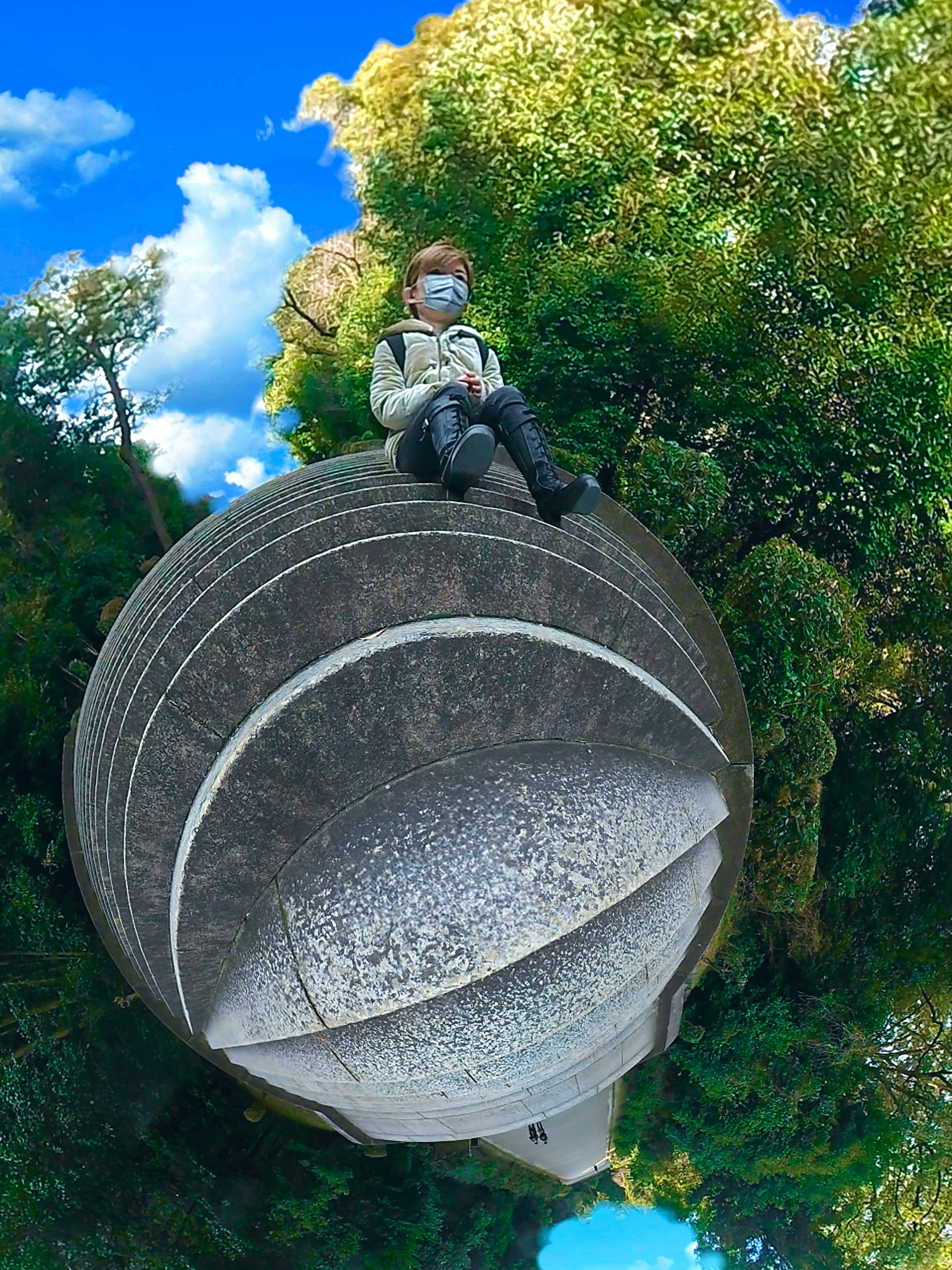 A person sitting on a round stone structure surrounded by lush greenery