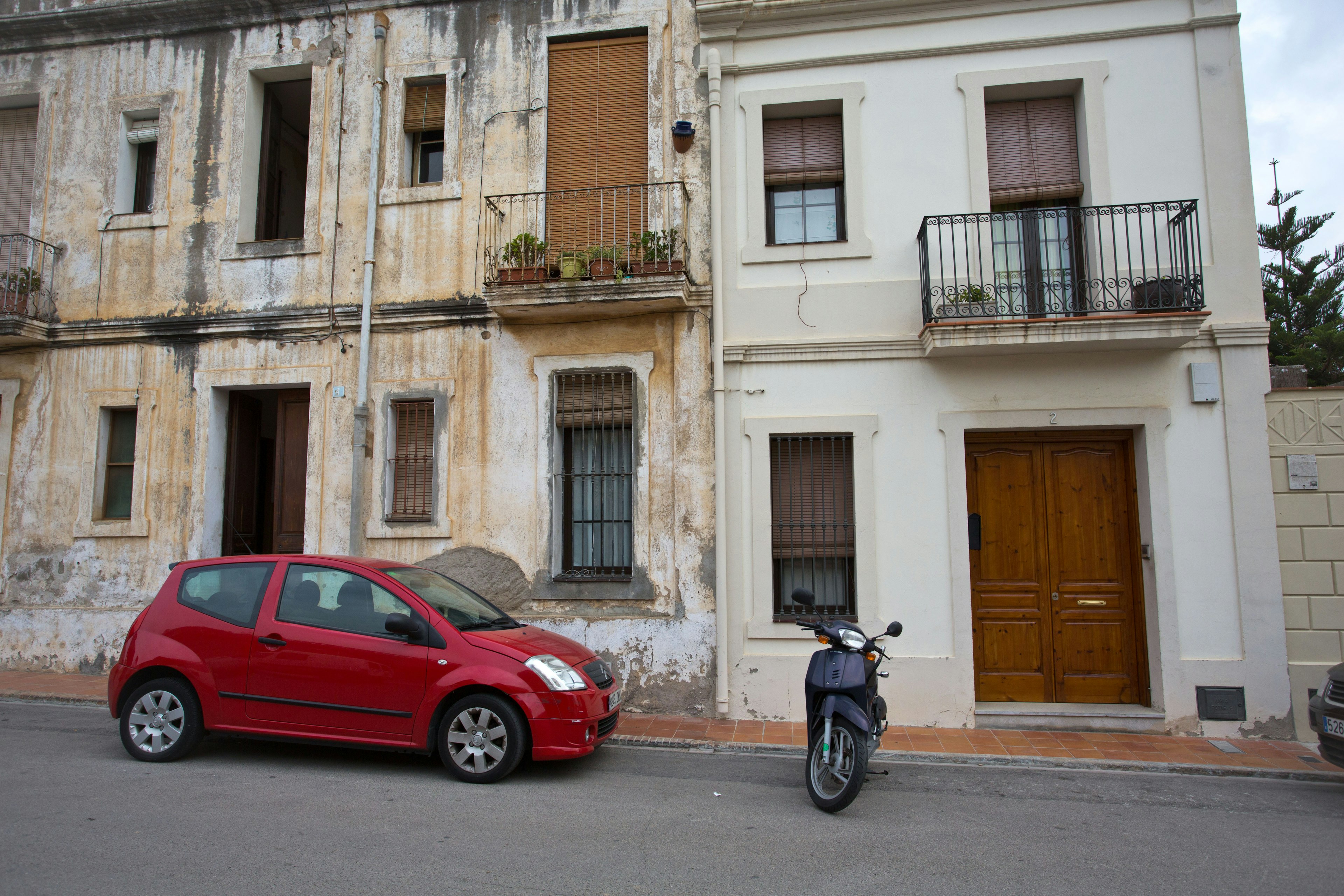 Une voiture rouge et un scooter garés sur une rue avec des bâtiments anciens et modernes