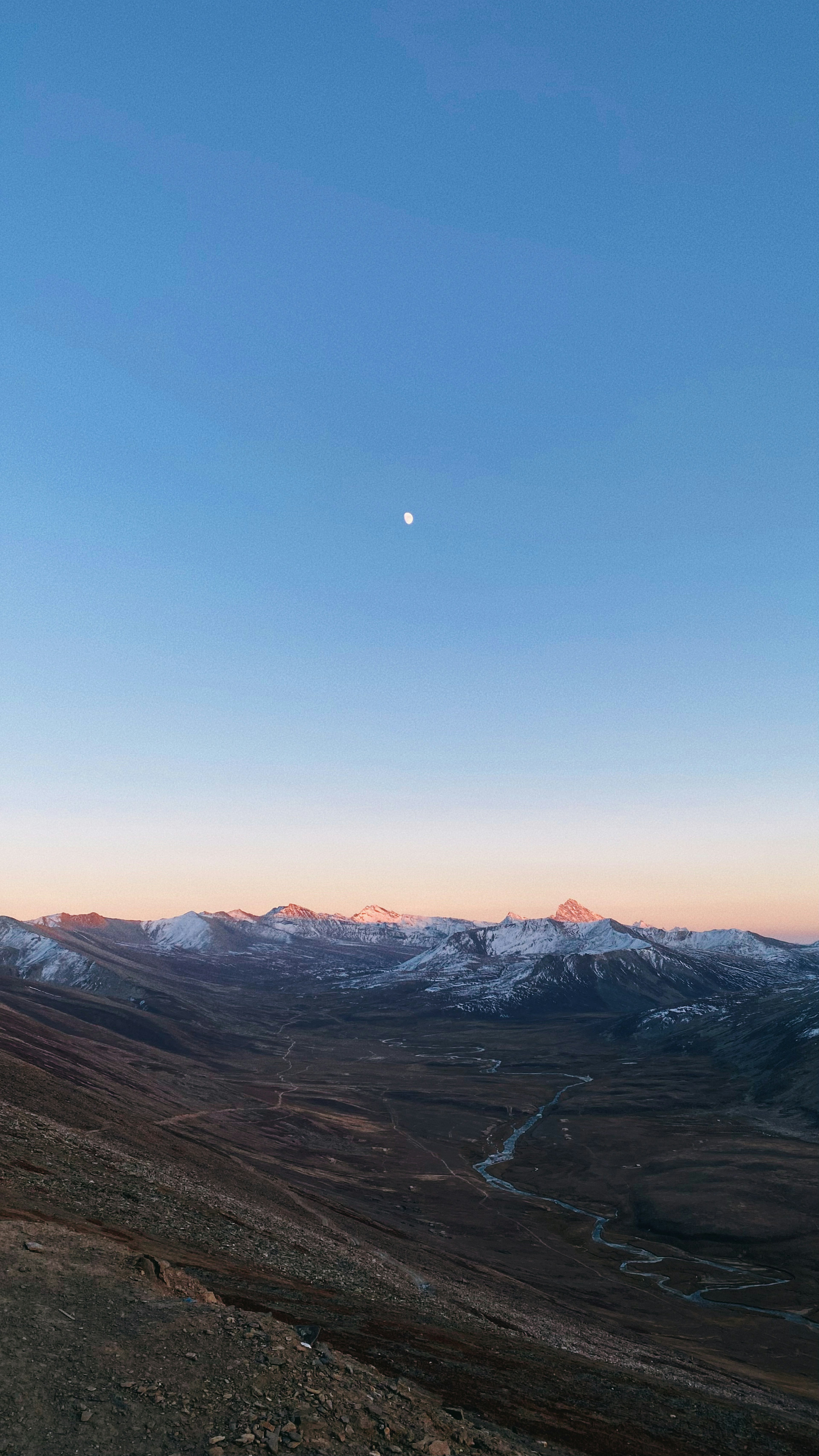 Luna nel cielo blu chiaro sopra le montagne innevate