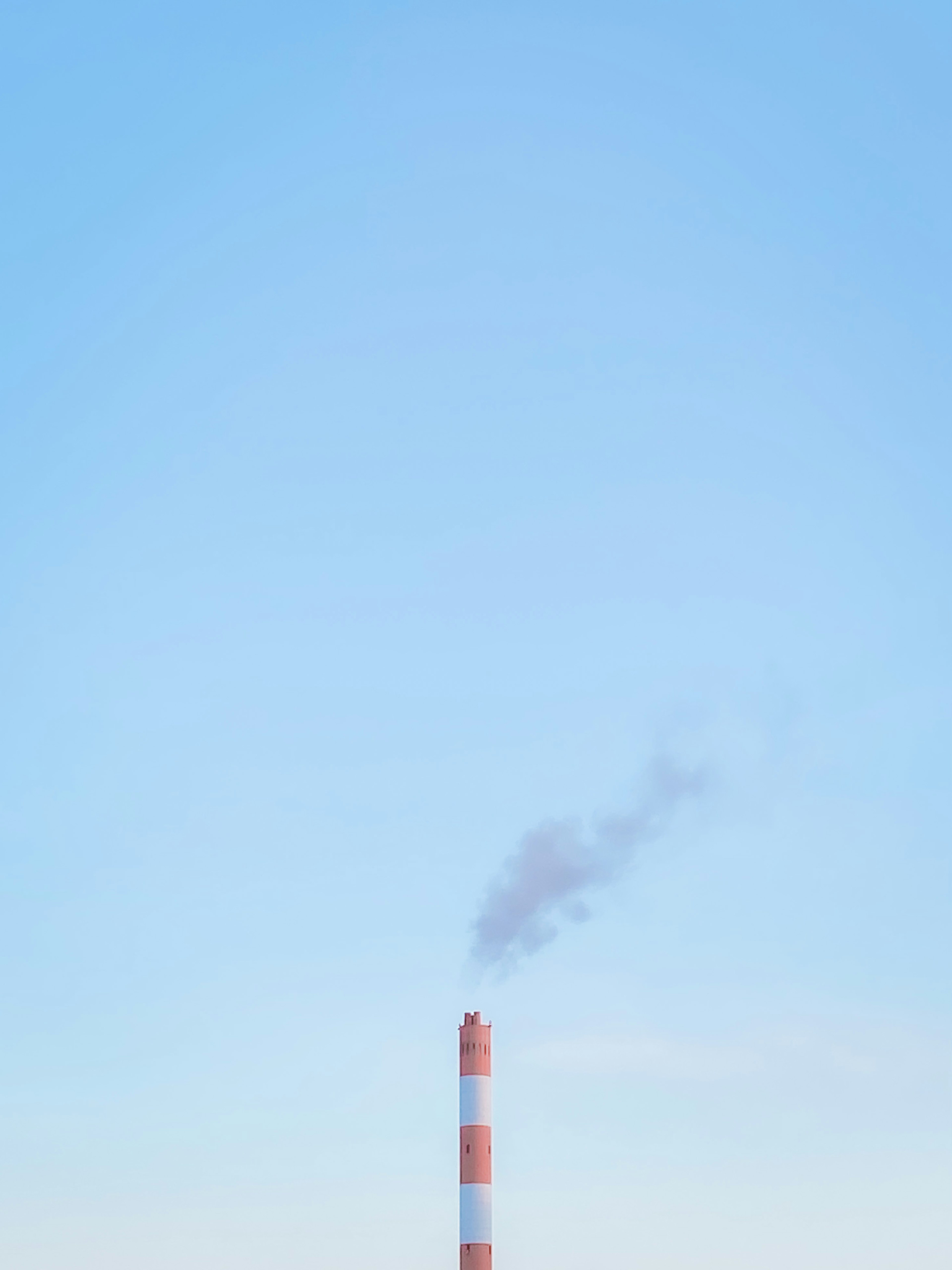 A red and white smokestack emitting smoke under a blue sky