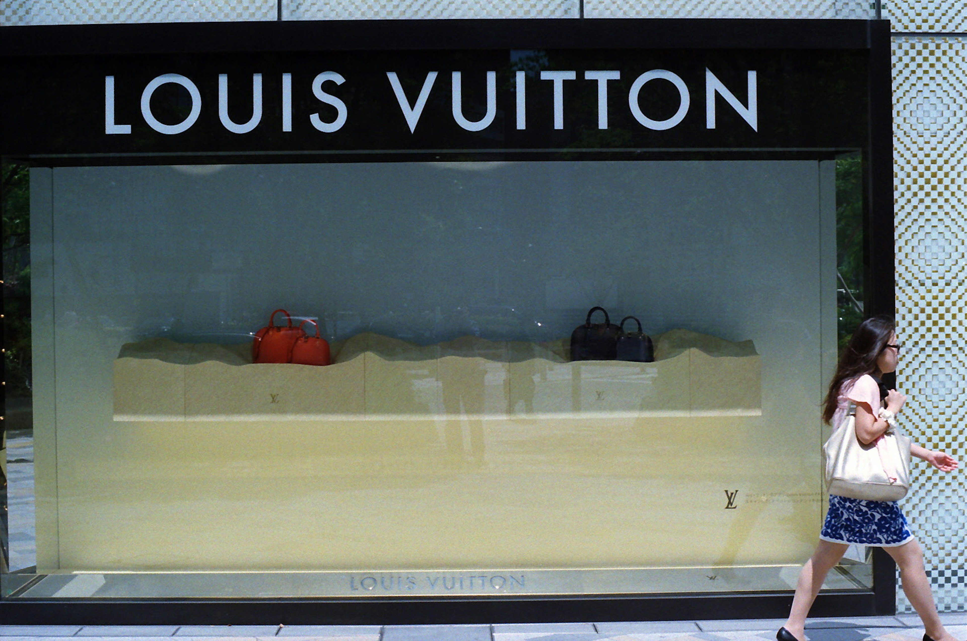 หน้าต่างร้าน Louis Vuitton แสดงกระเป๋าและผู้หญิงที่เดินผ่าน