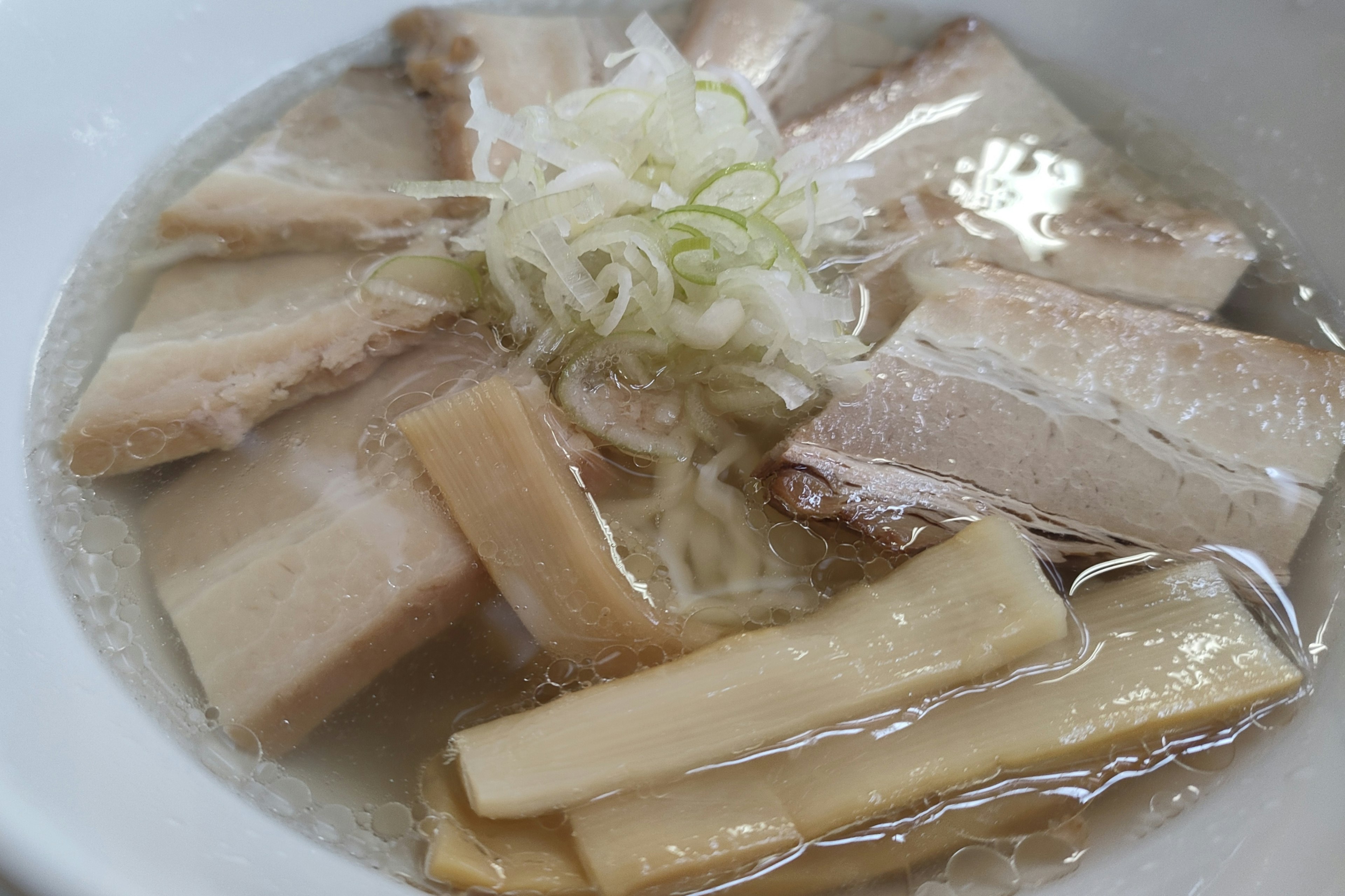 豚肉のスライスとネギがトッピングされたラーメンのスープ