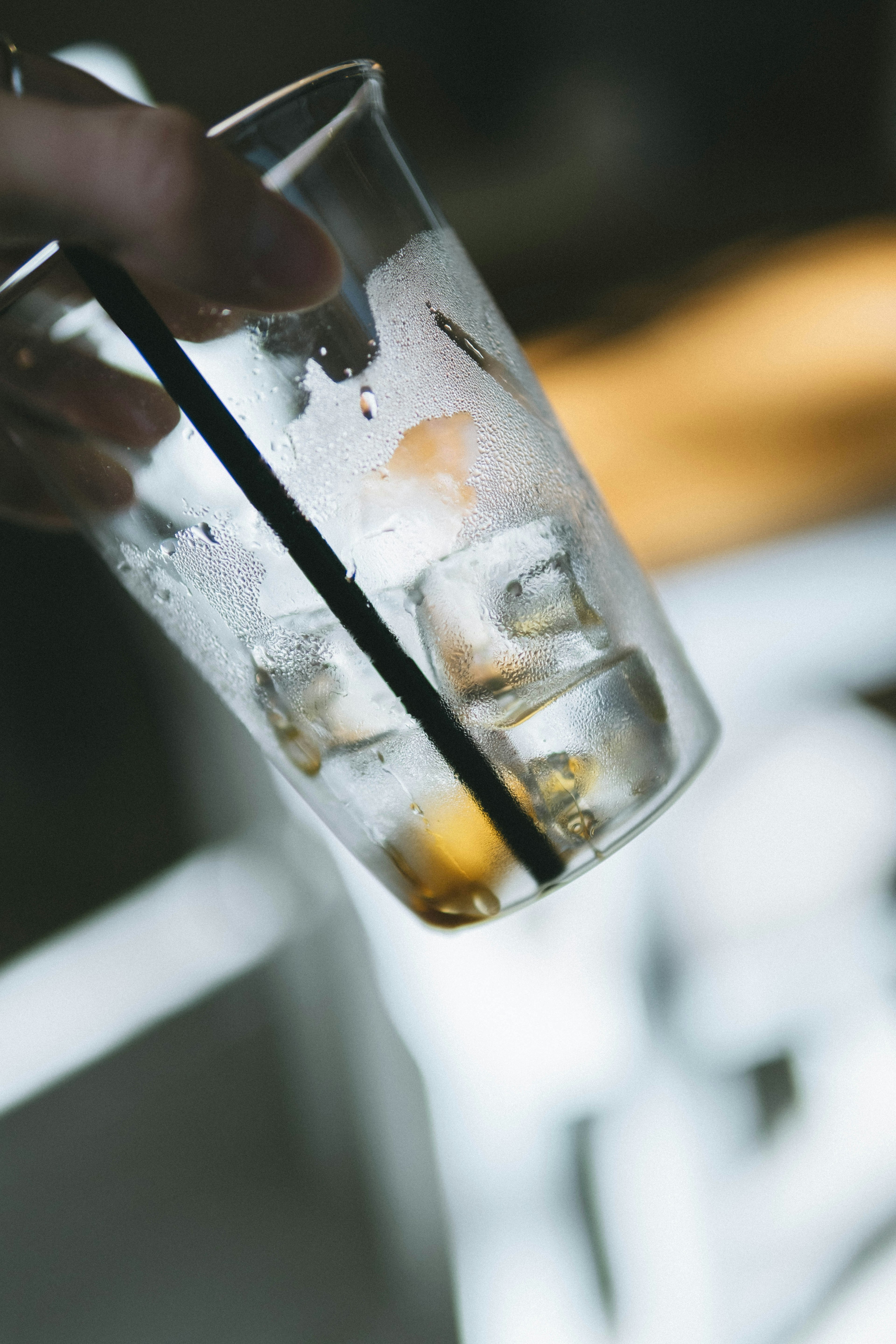 Una mano sosteniendo un vaso transparente con hielo y una pajita negra