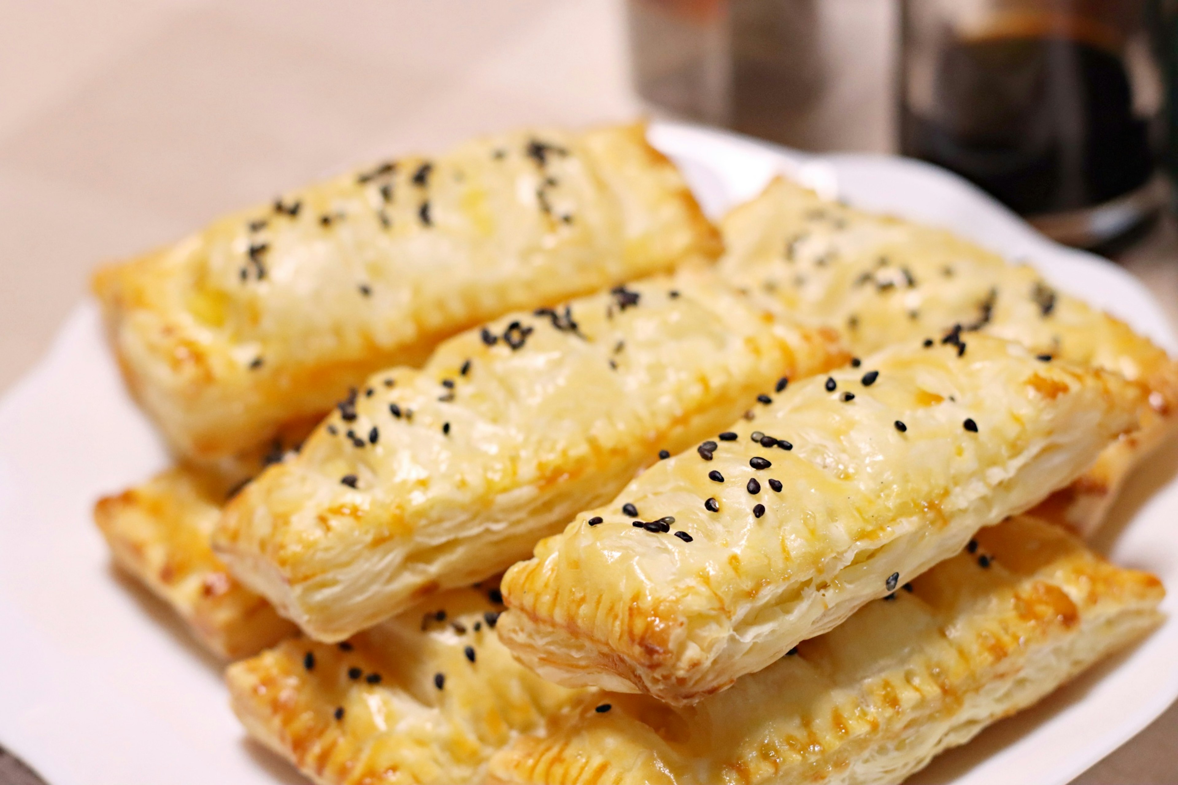 A stack of flaky pastries topped with black sesame seeds on a white plate