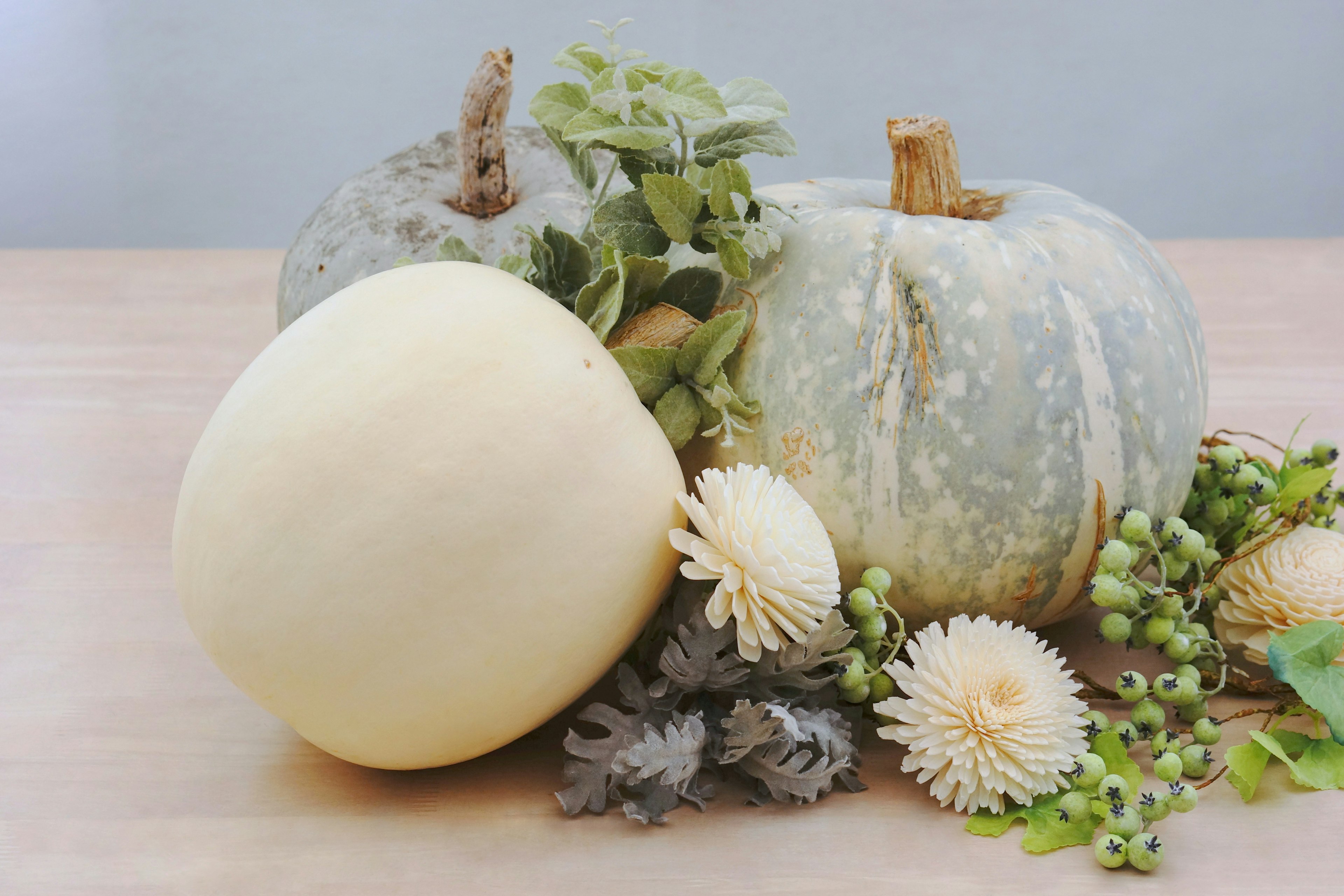 Un gruppo di zucche bianche e verdi accompagnato da foglie e fiori