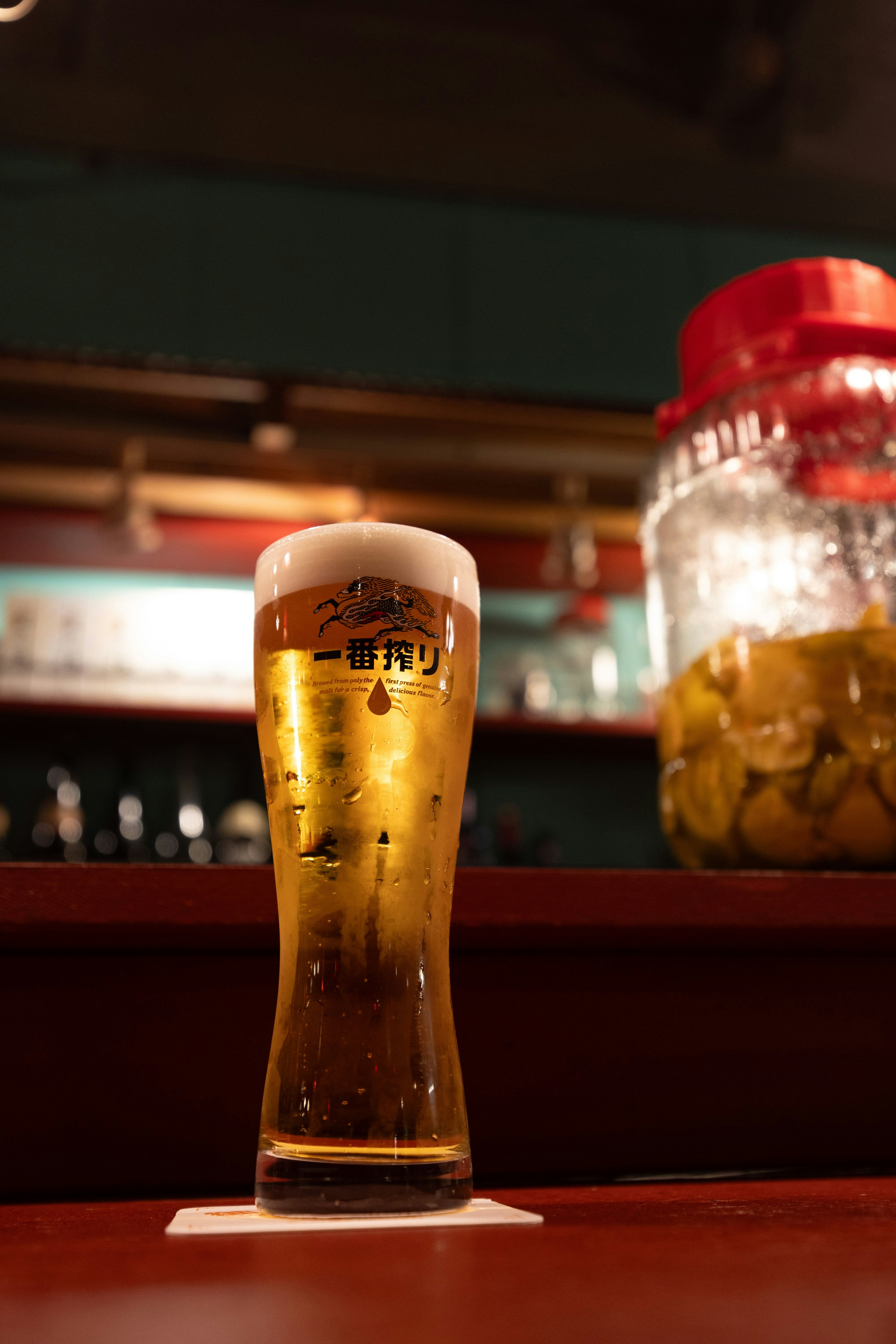 Ein Glas Bier auf einem Tisch mit einem Glas im Hintergrund, das eine Bar-Atmosphäre zeigt