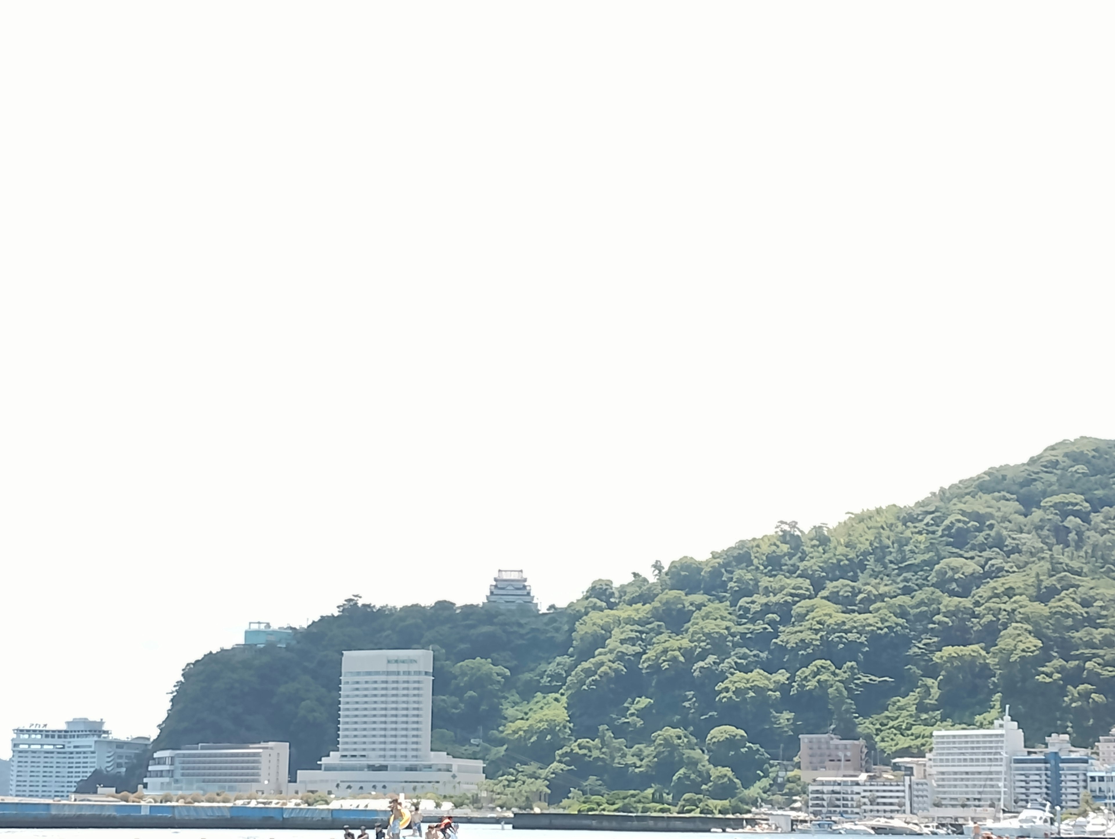 Modern buildings alongside a lush green mountain by the sea