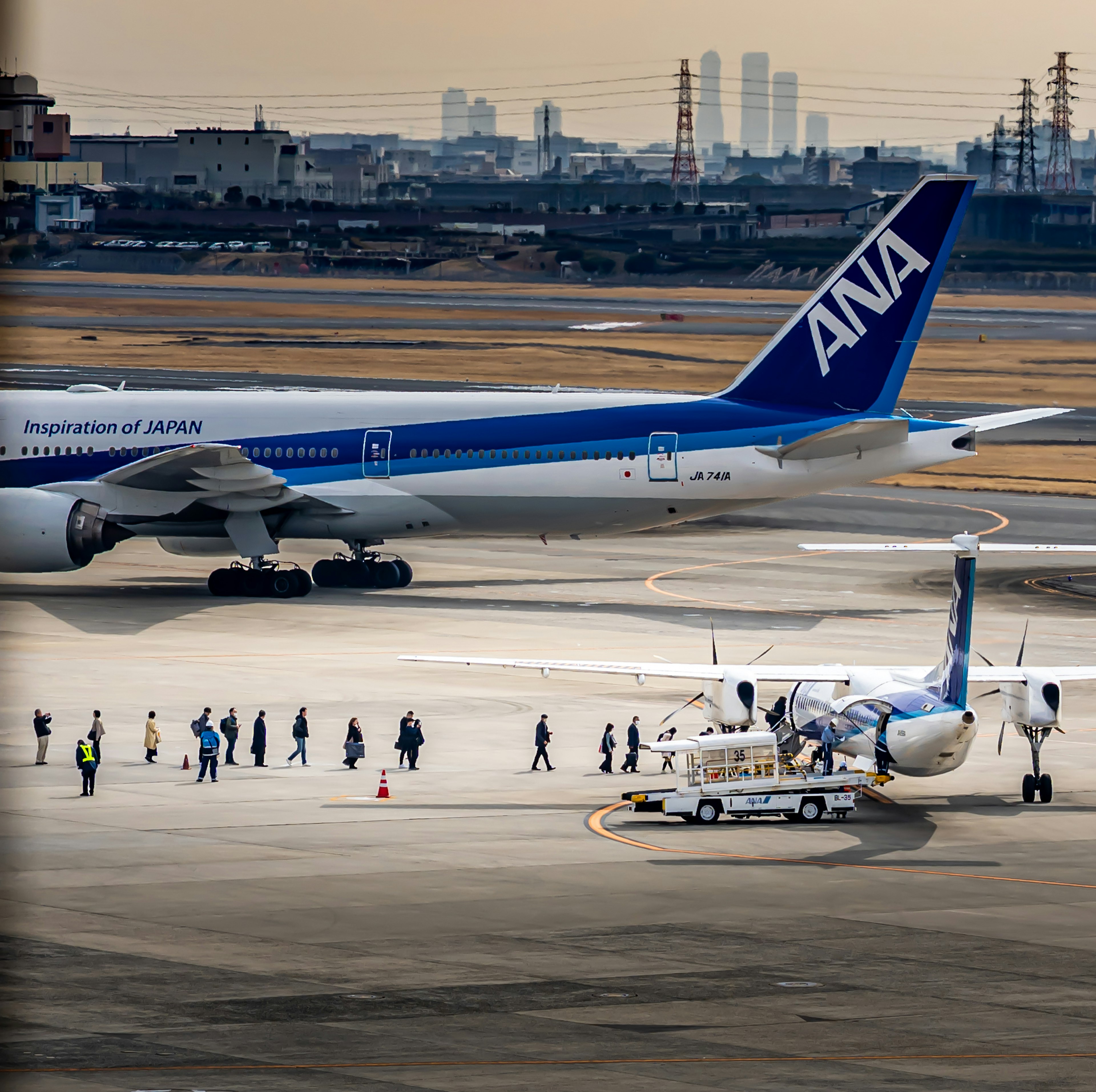 Avión de pasajeros de ANA y un avión más pequeño en la pista con personas abordando