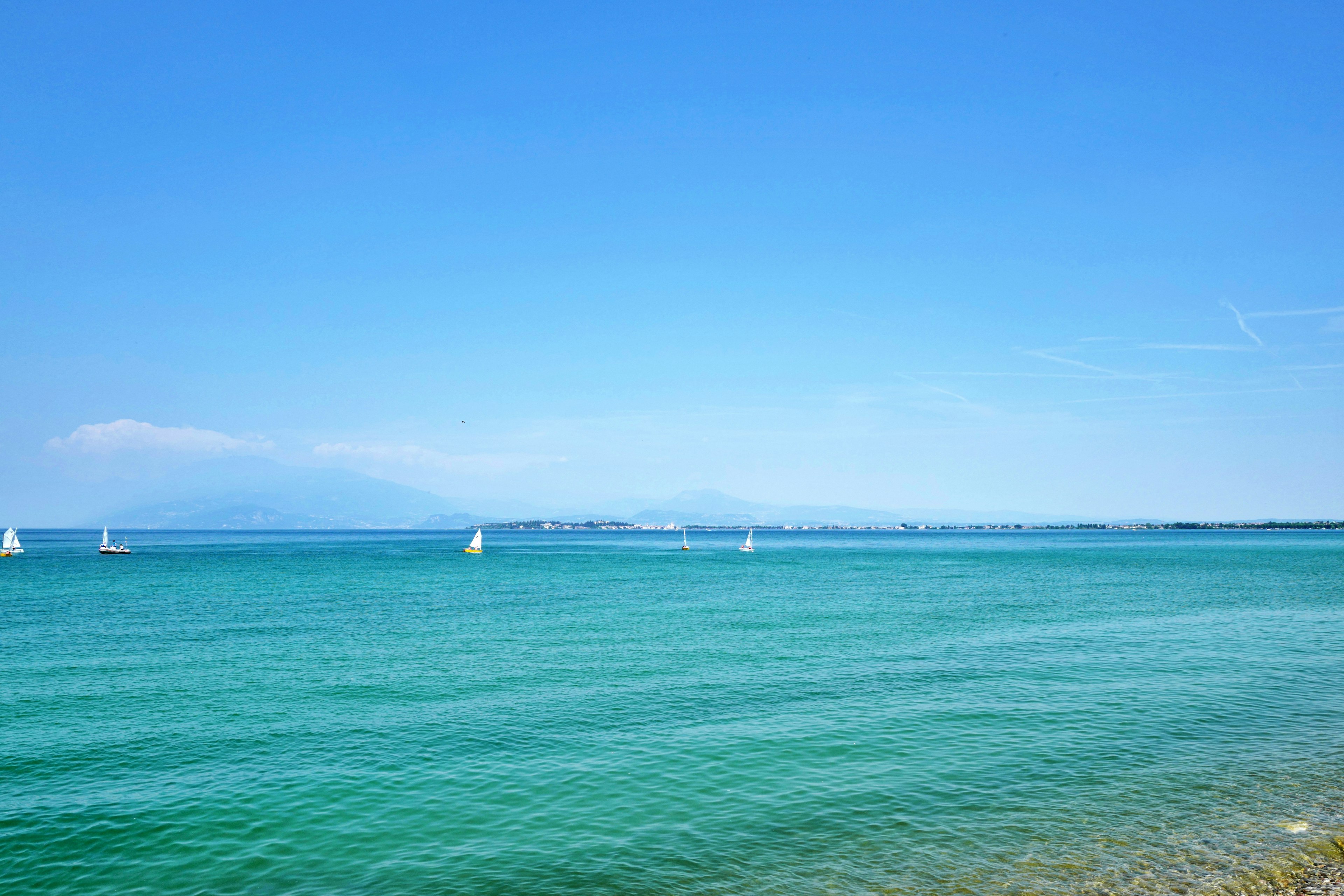 Clear blue sky with calm sea and white sailboats in the distance