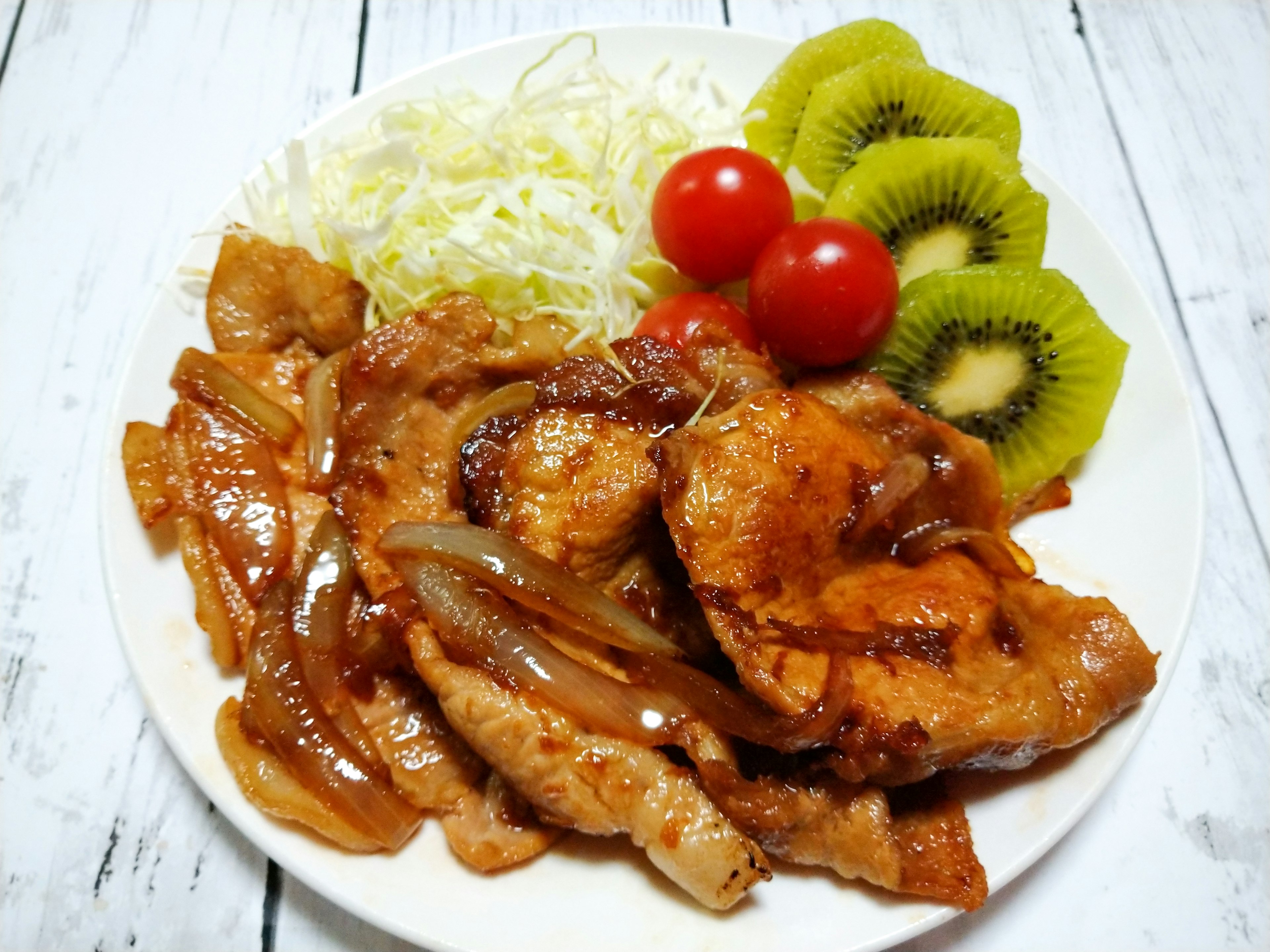 A plate of pork dish served with salad and colorful vegetables