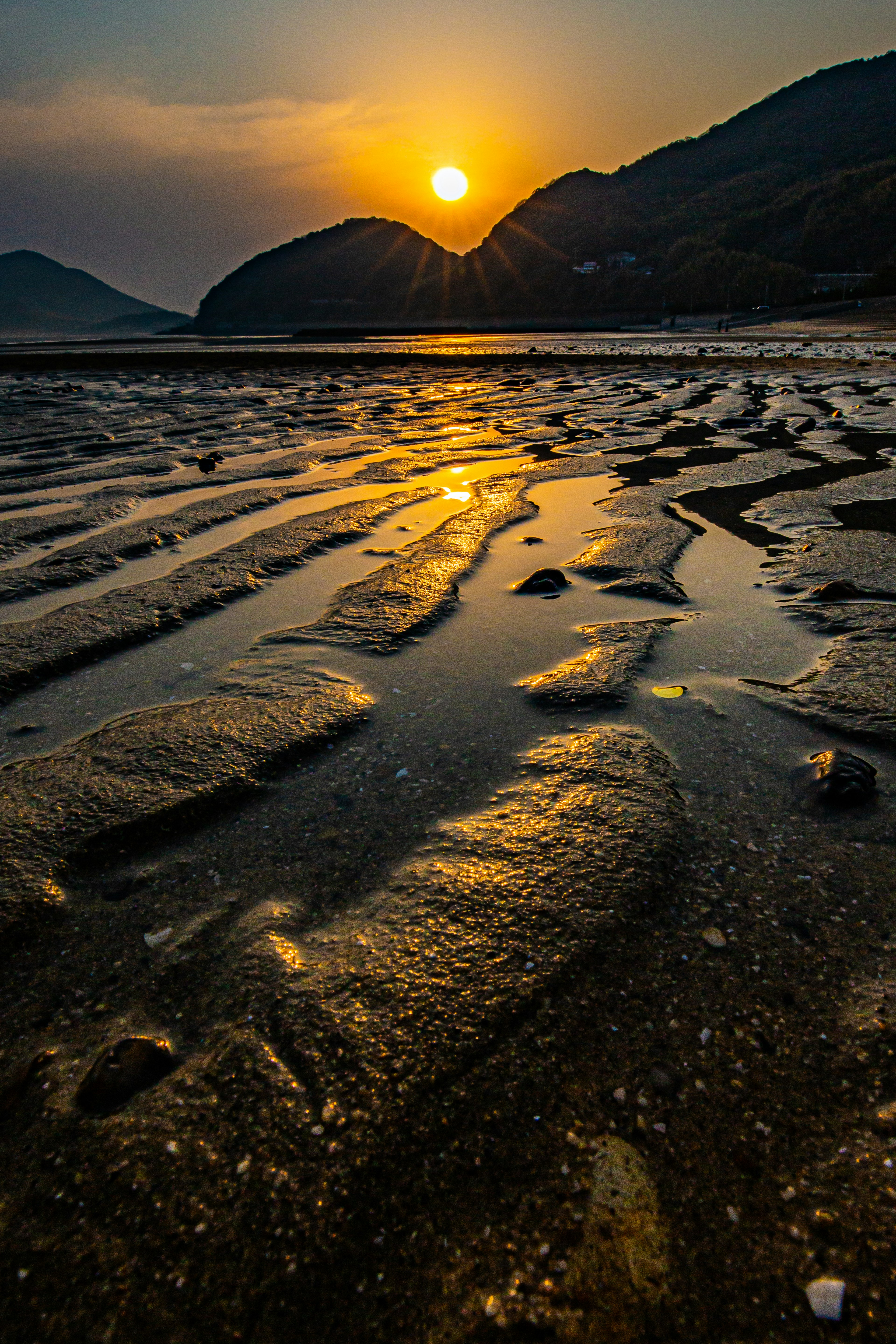 Paesaggio costiero al tramonto con montagne sullo sfondo e motivi di sabbia bagnata riflettenti