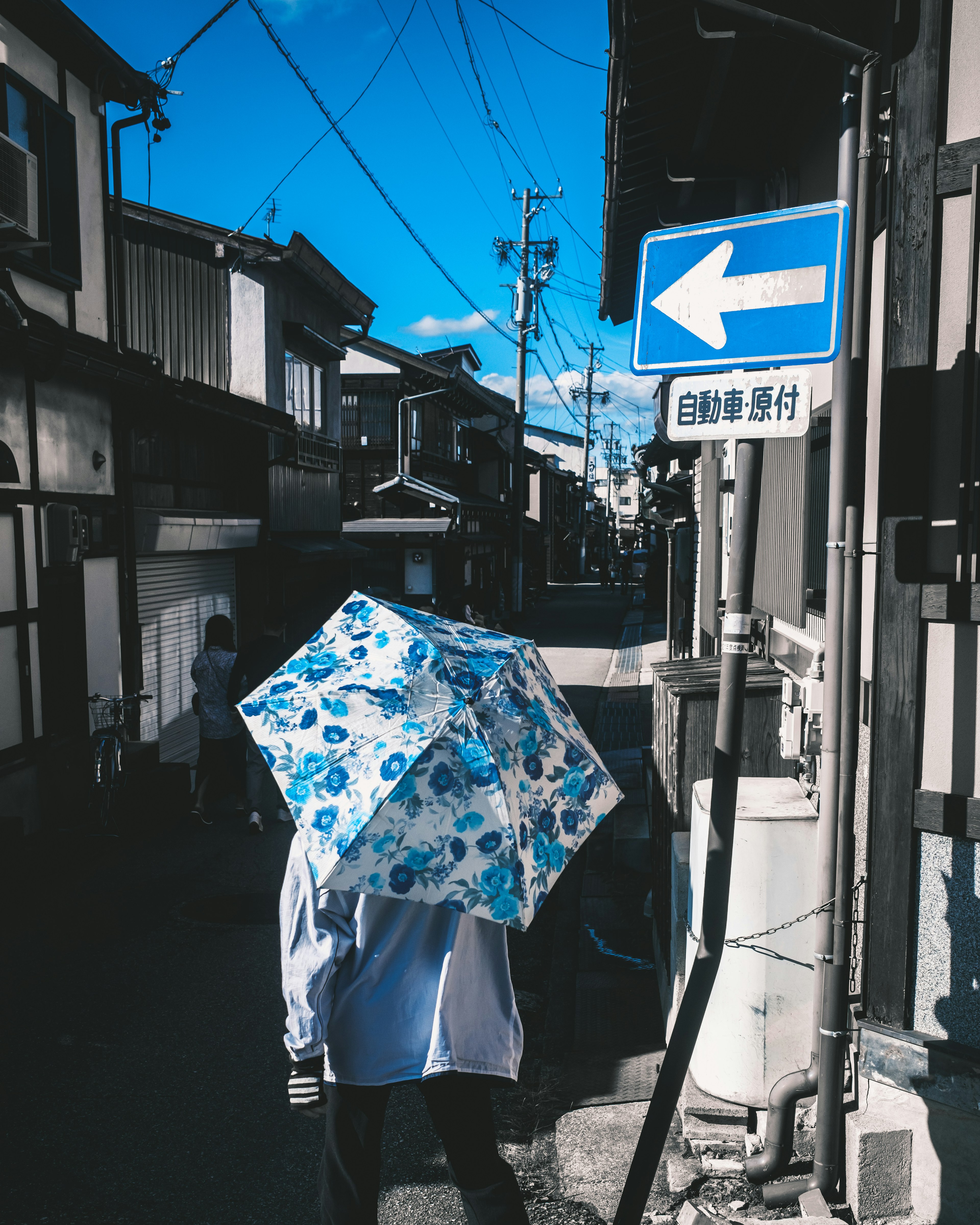 Una persona caminando en una calle antigua bajo un cielo azul con un paraguas decorado