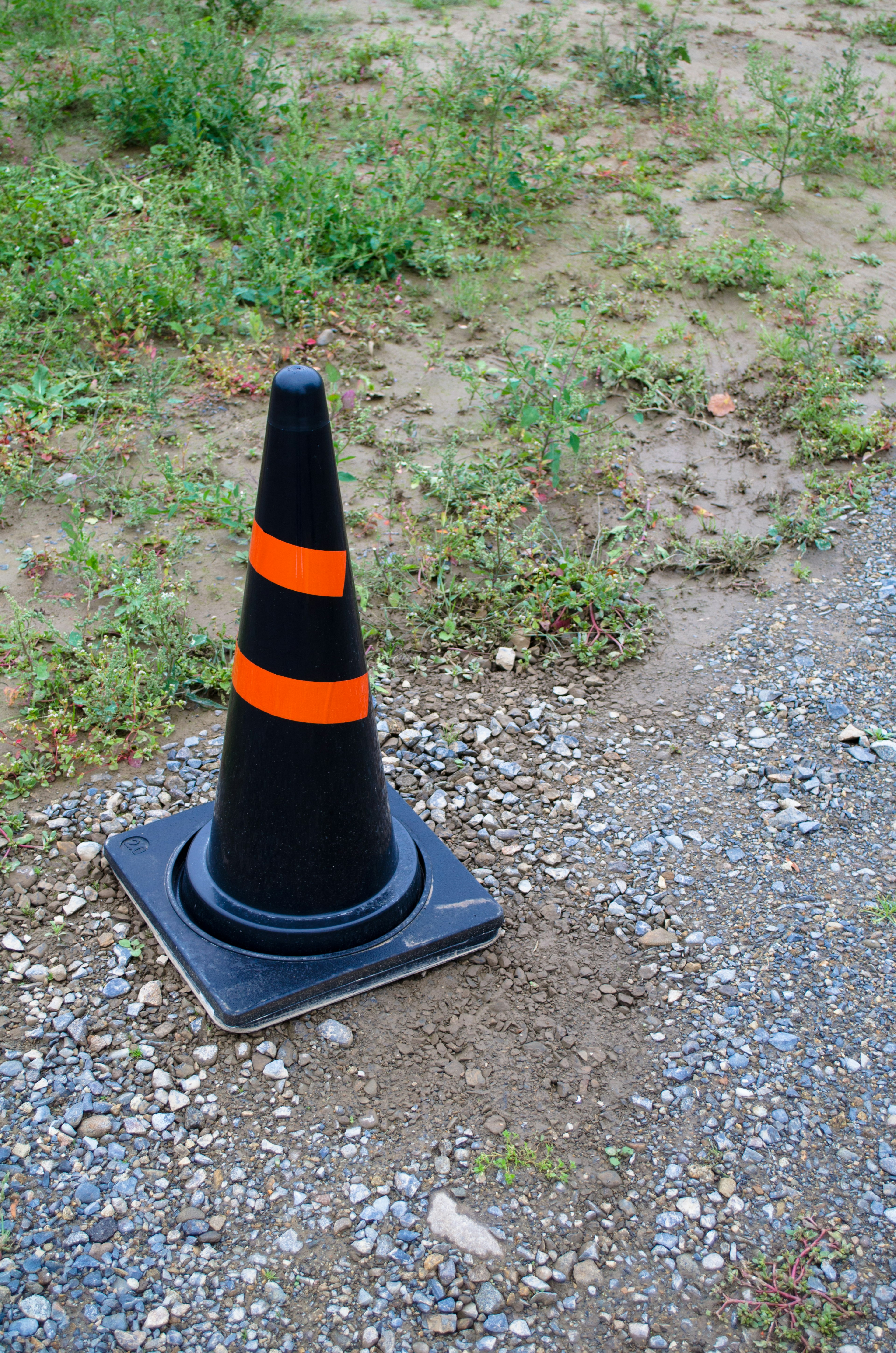 A black traffic cone with orange stripes standing near grassy area