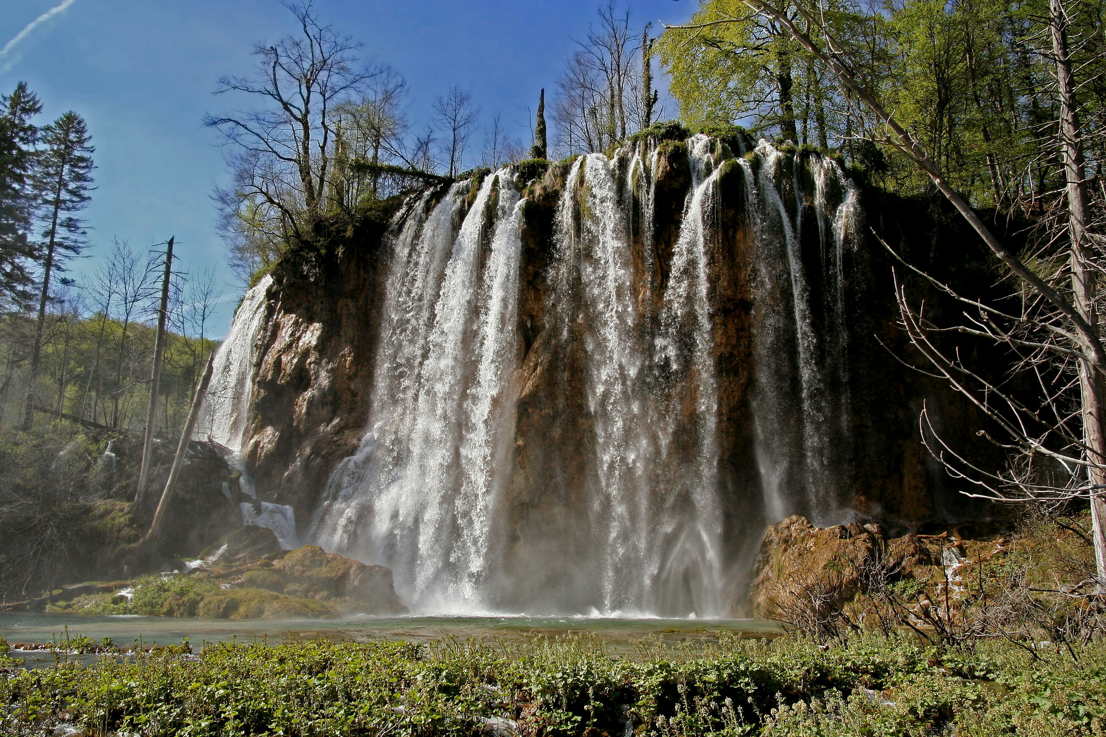 Magnifique paysage de cascade avec de l'eau qui coule sous un ciel bleu et de l'herbe verte