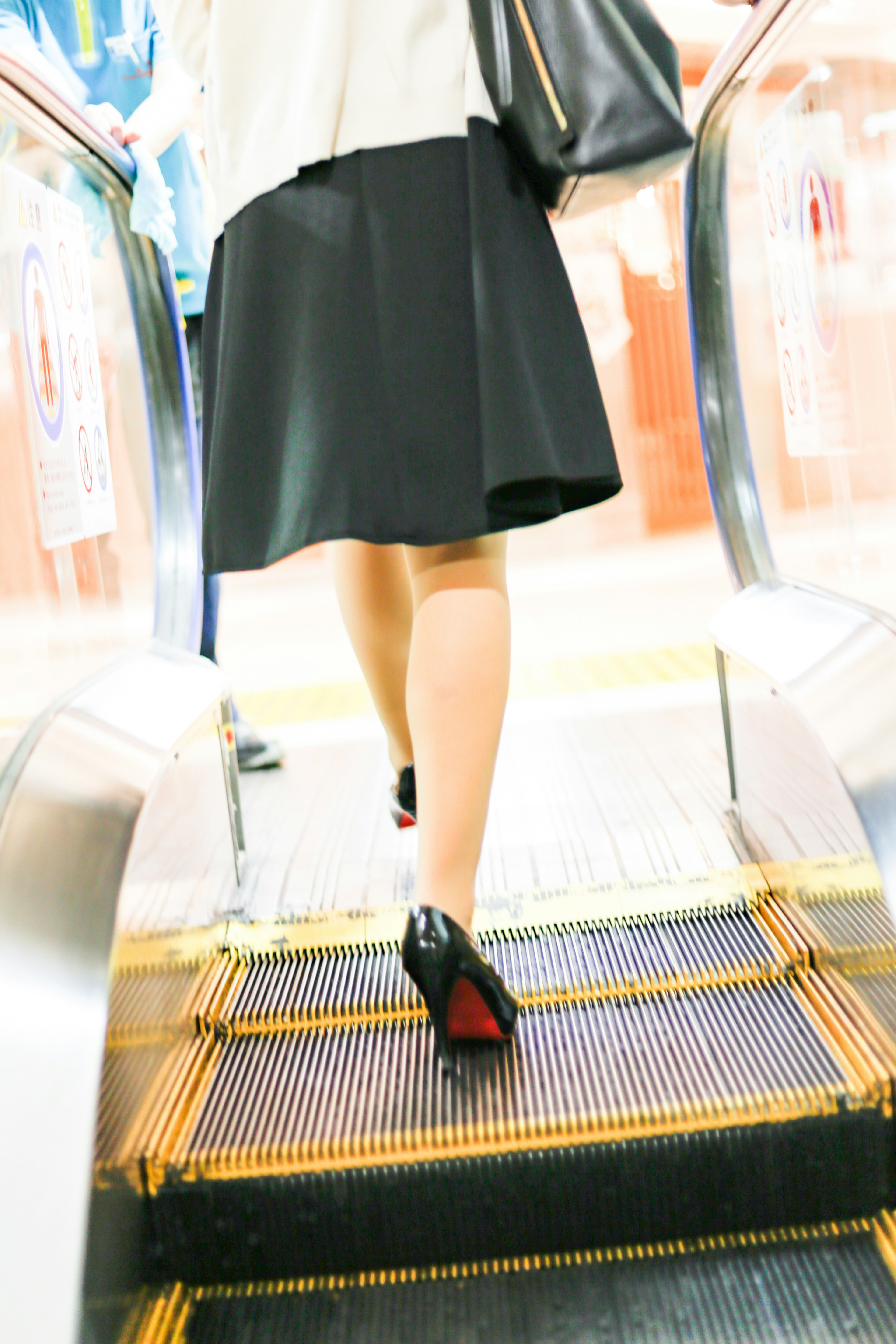 Mujer subiendo una escalera mecánica con una falda negra y tacones rojos