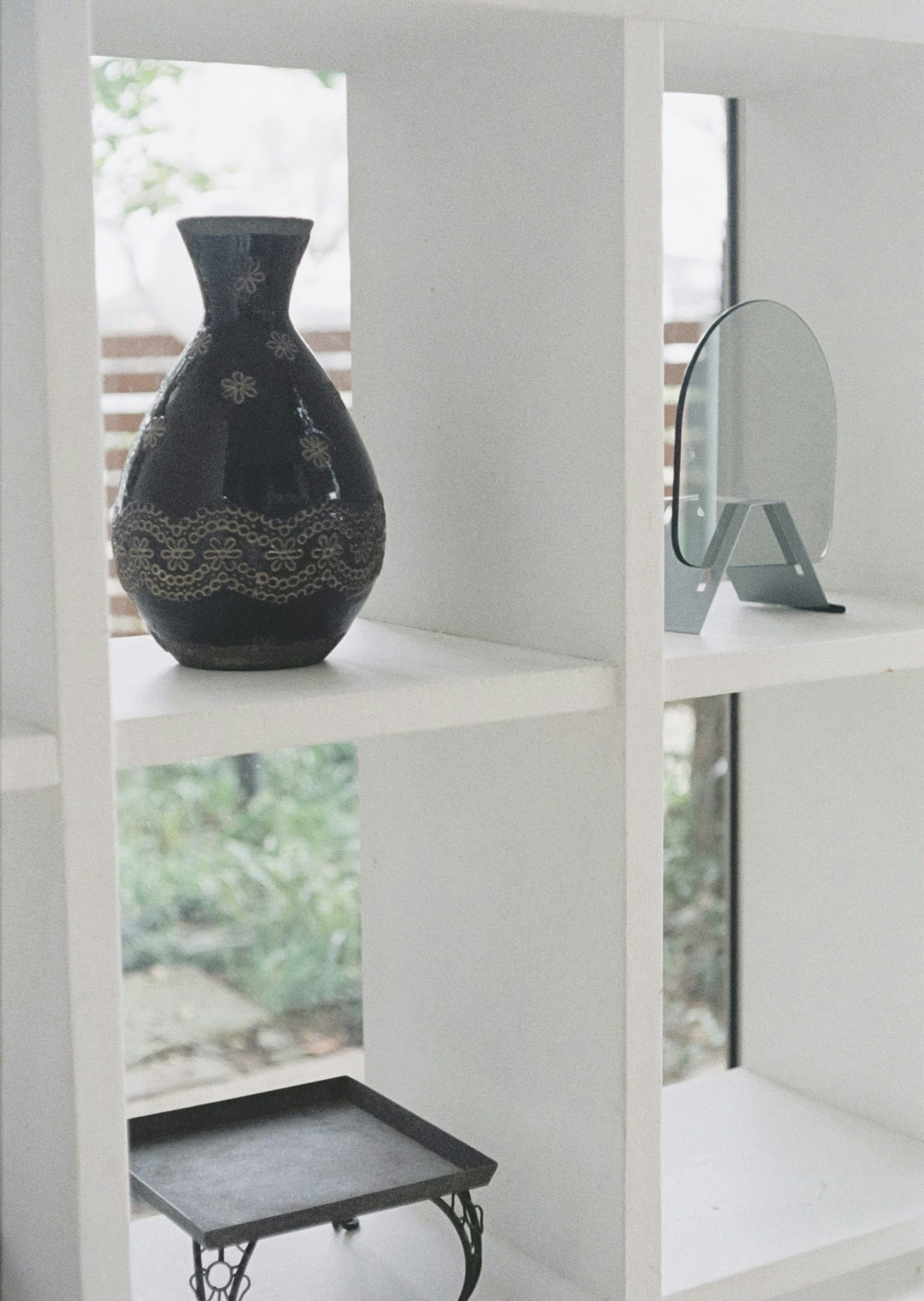 A black vase and a mirror on a white shelf in a serene interior