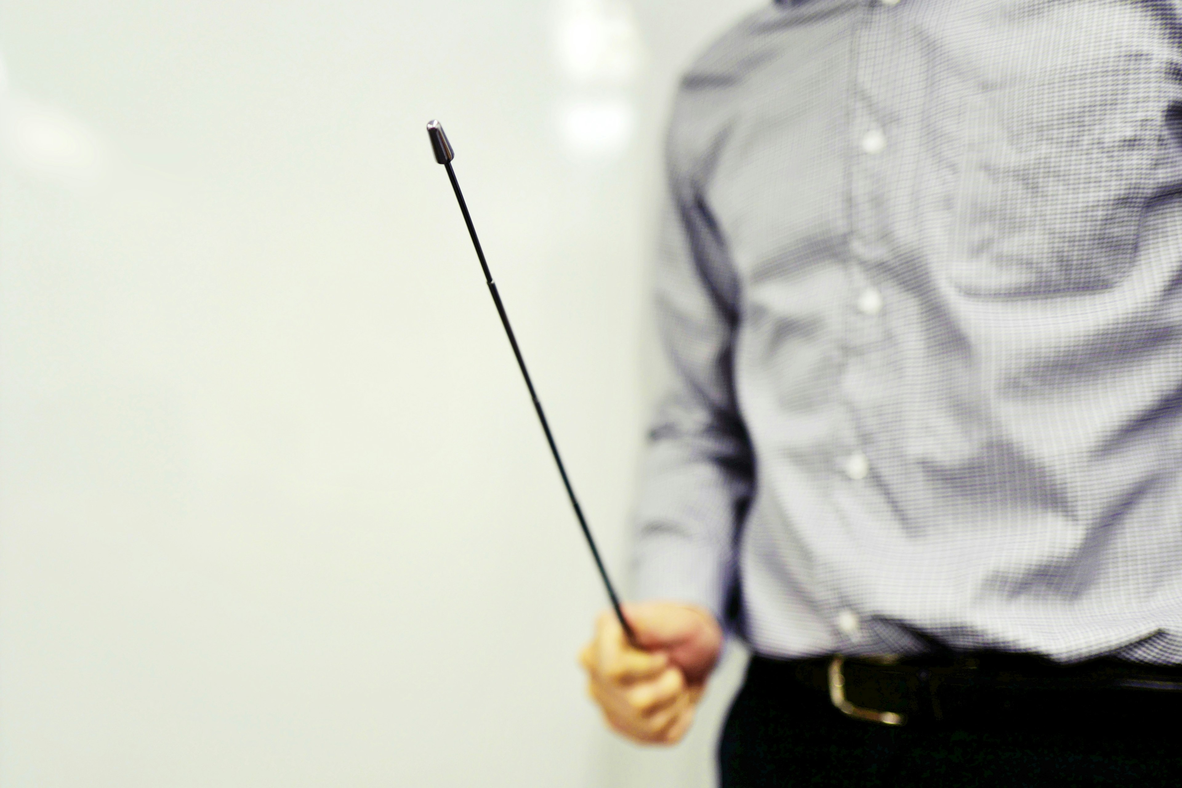 A man in a dress shirt holding a pointer in front of a whiteboard