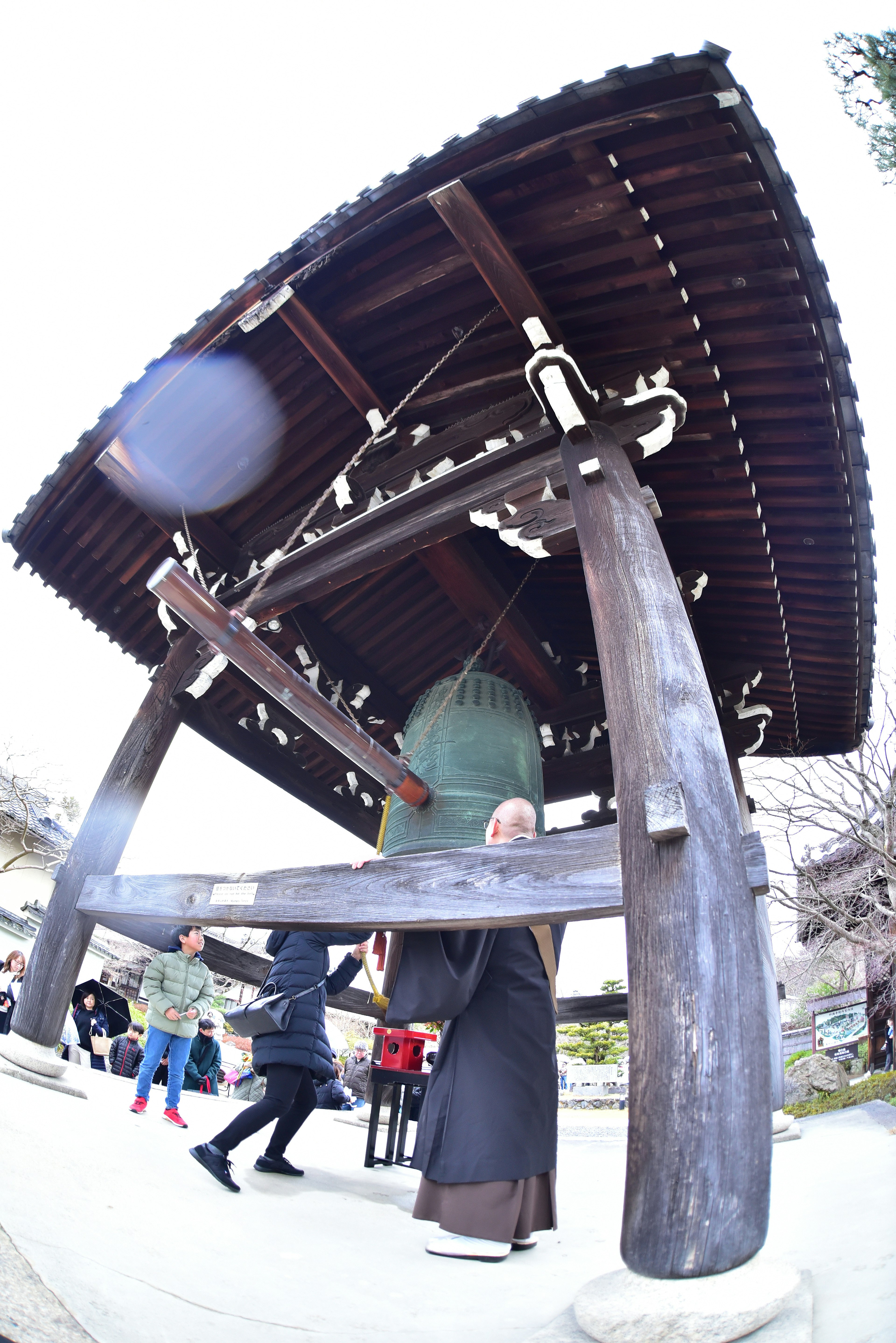 寺院の鐘楼の下にいる僧侶と訪問者たちの姿