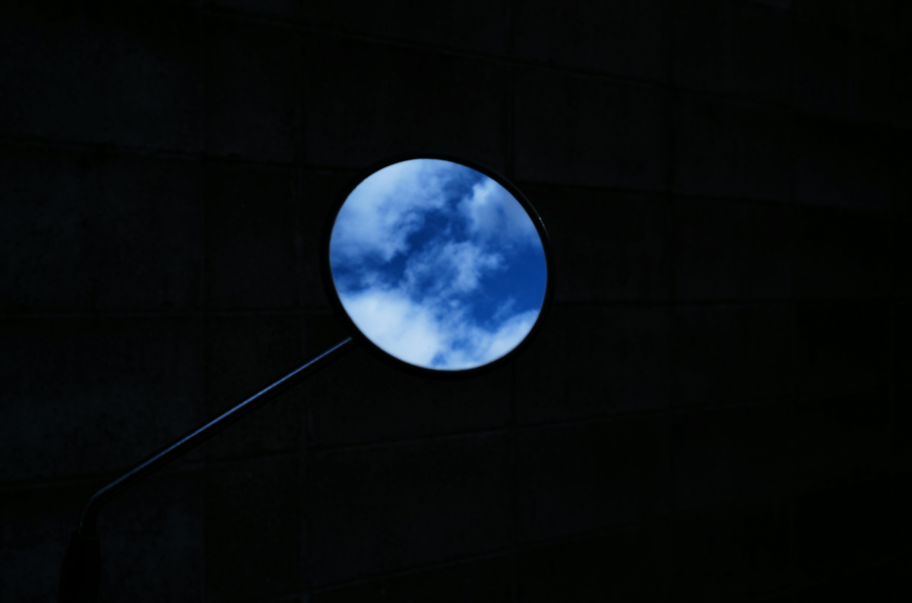 Circular mirror reflecting blue sky and white clouds against dark background