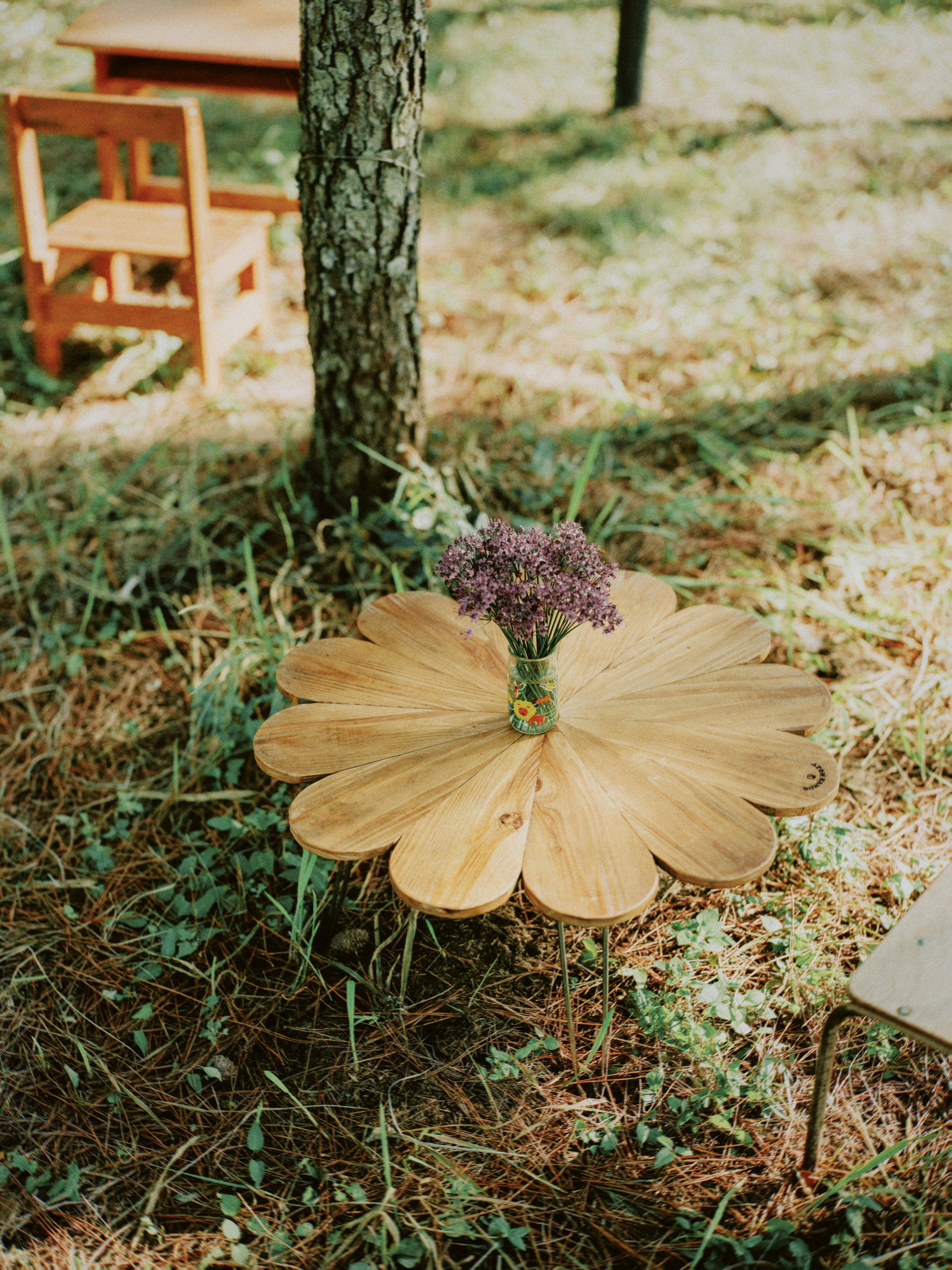 A wooden table resembling a flower with purple flowers placed on it in a natural setting