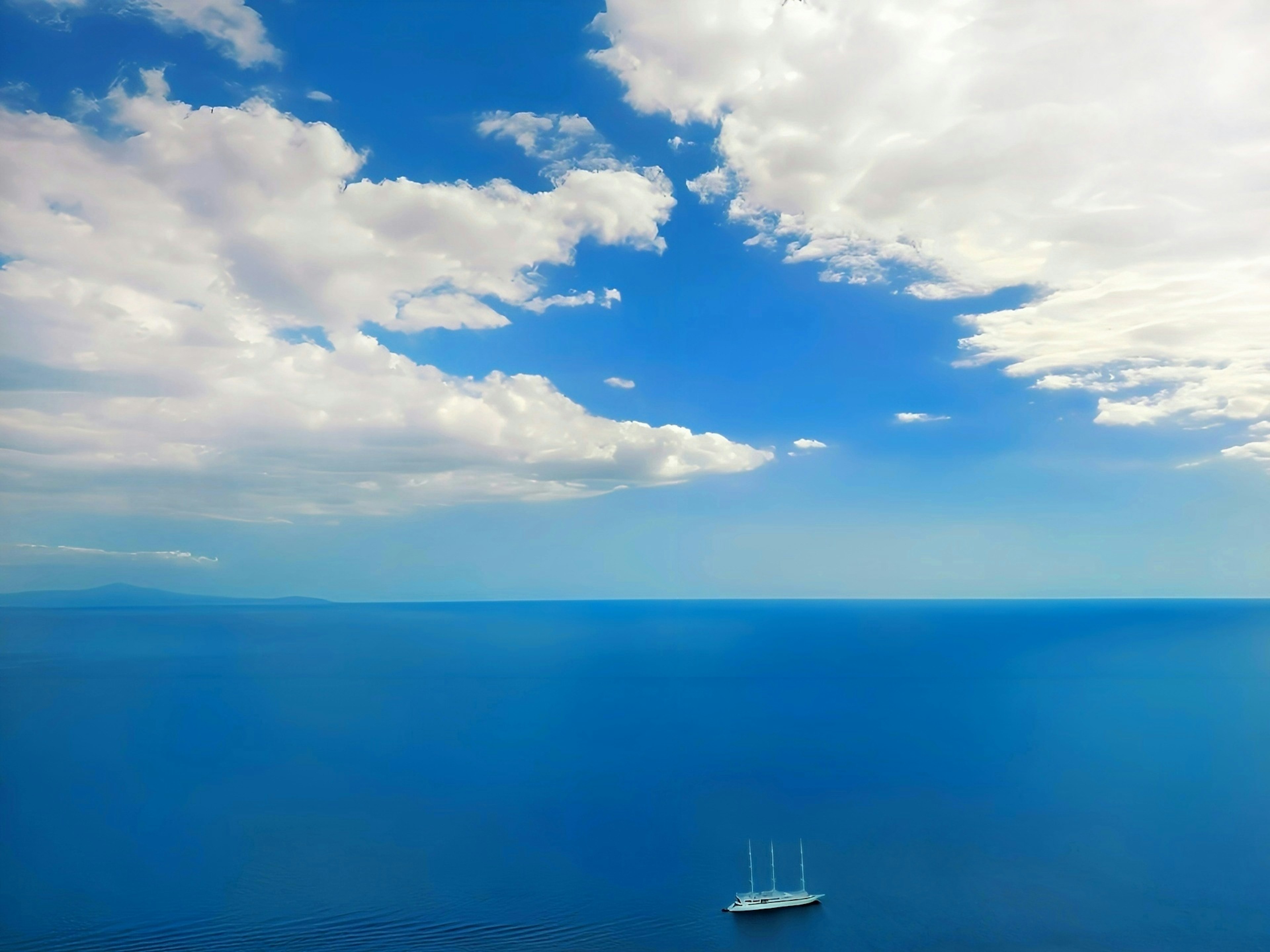 Une vue sereine de l'océan bleu et du ciel avec des nuages blancs un voilier au loin