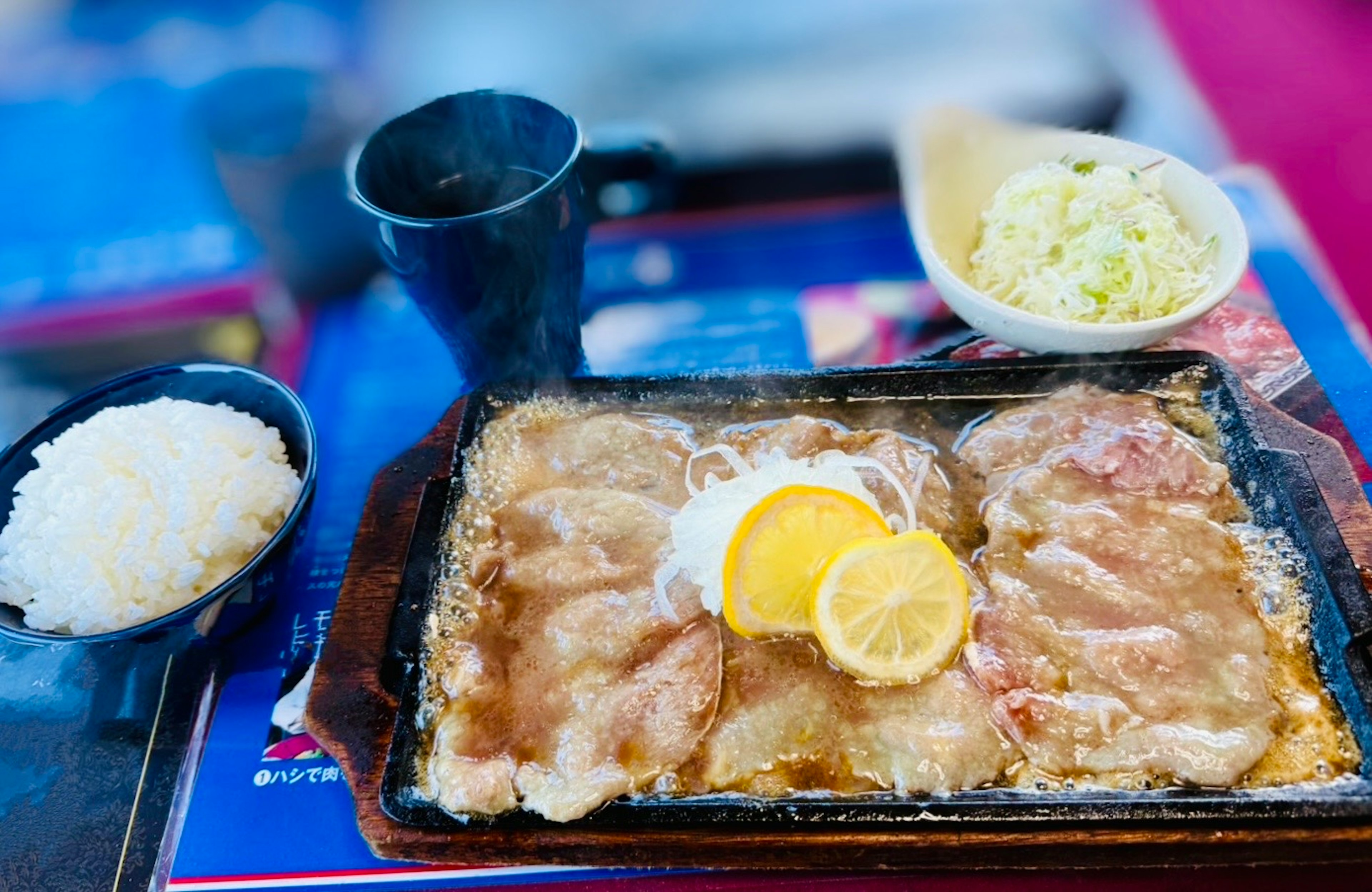 Sizzling pork dish with lemon served on a hot plate accompanied by rice and cabbage