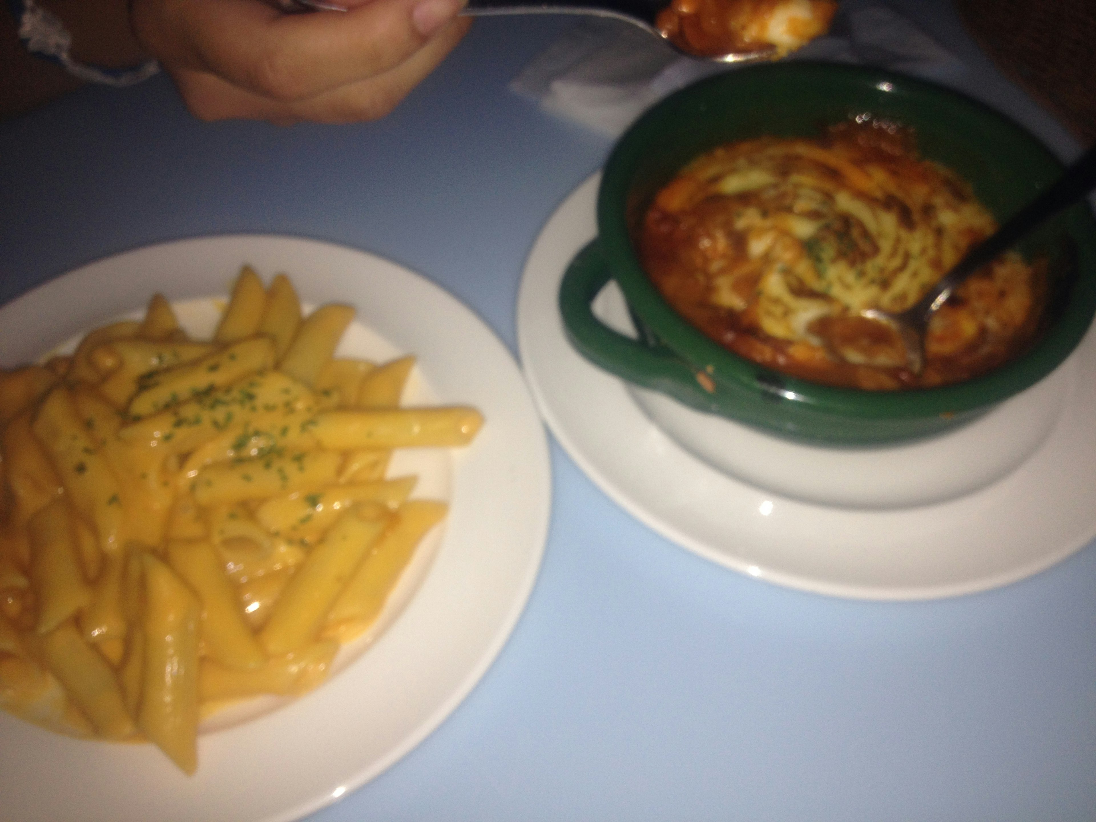 Pasta penne en primer plano con un plato de queso derretido en un tazón verde al fondo