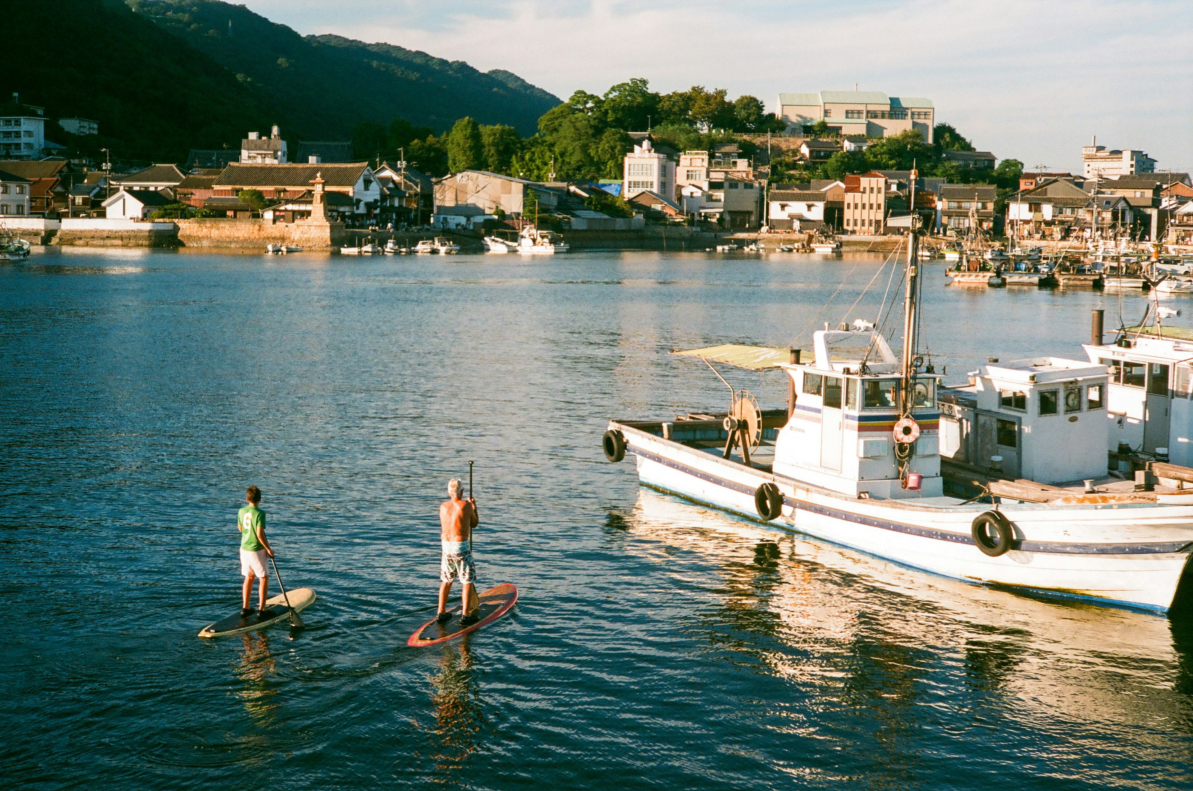 Hai người đang tận hưởng paddleboarding trên mặt nước yên tĩnh với một thị trấn yên tĩnh ở phía sau