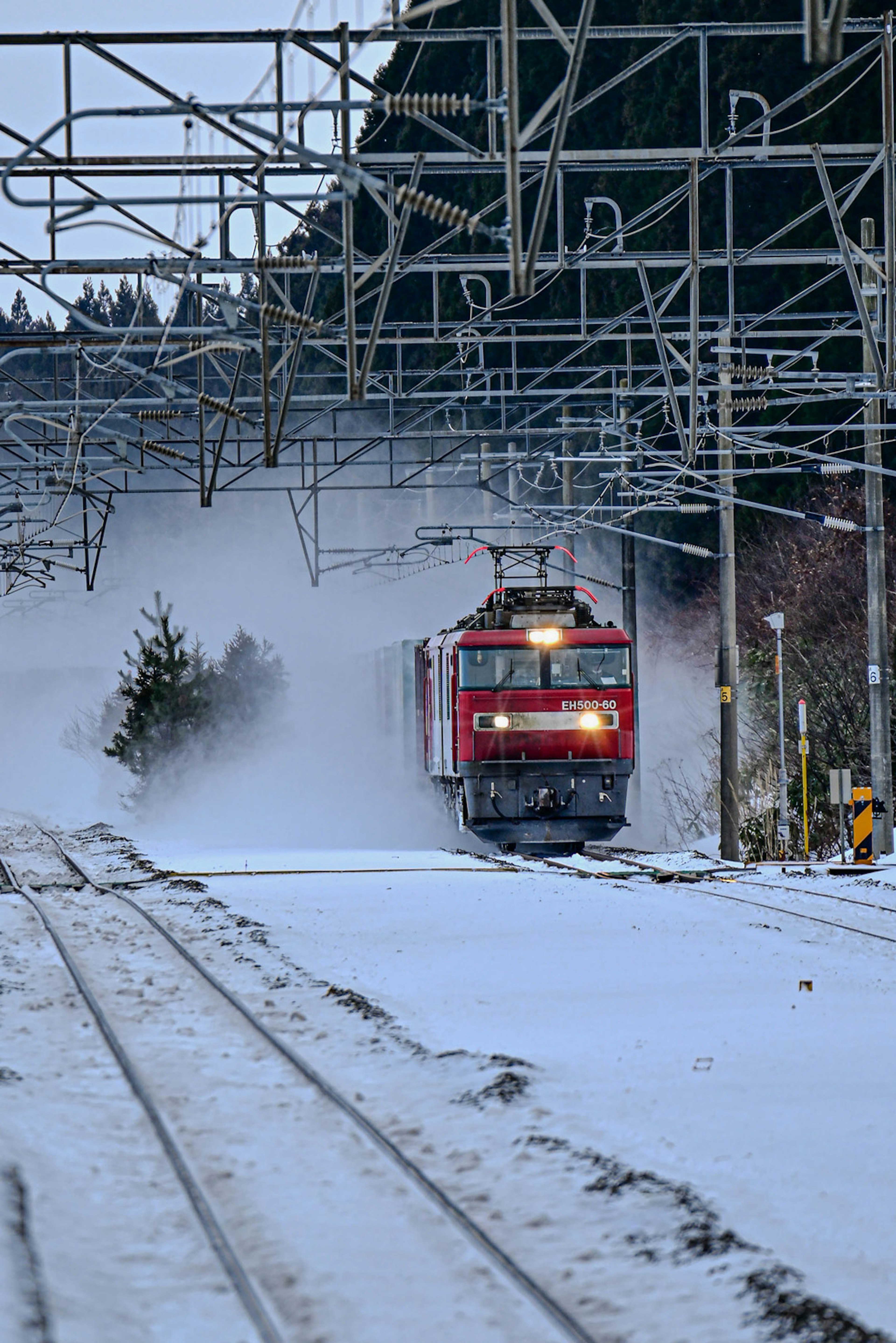 Roter Zug, der durch Schnee fährt, umgeben von Stromleitungen