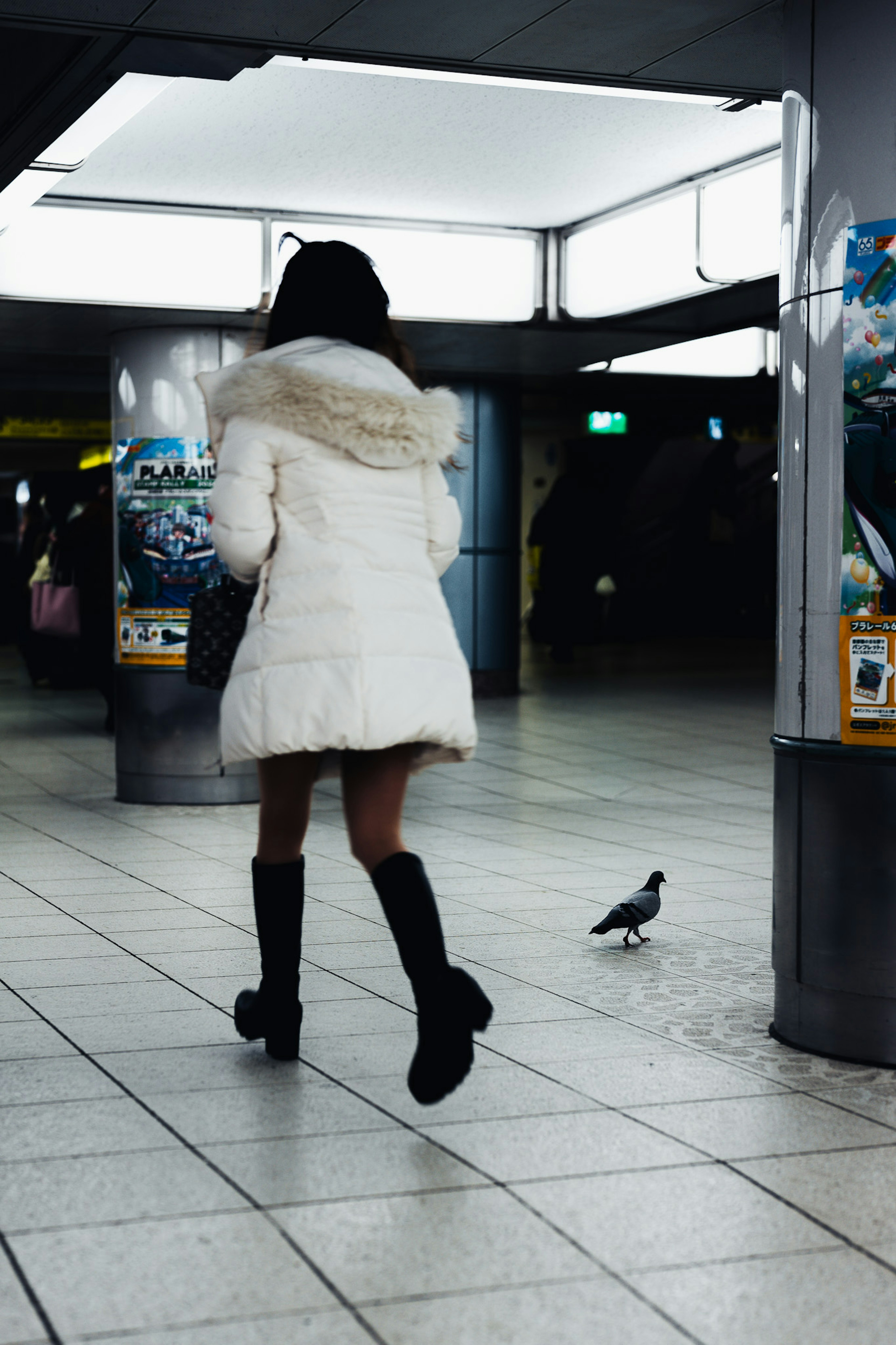 白いコートを着た女性が地下鉄駅を歩いている 鳩が近くにいる