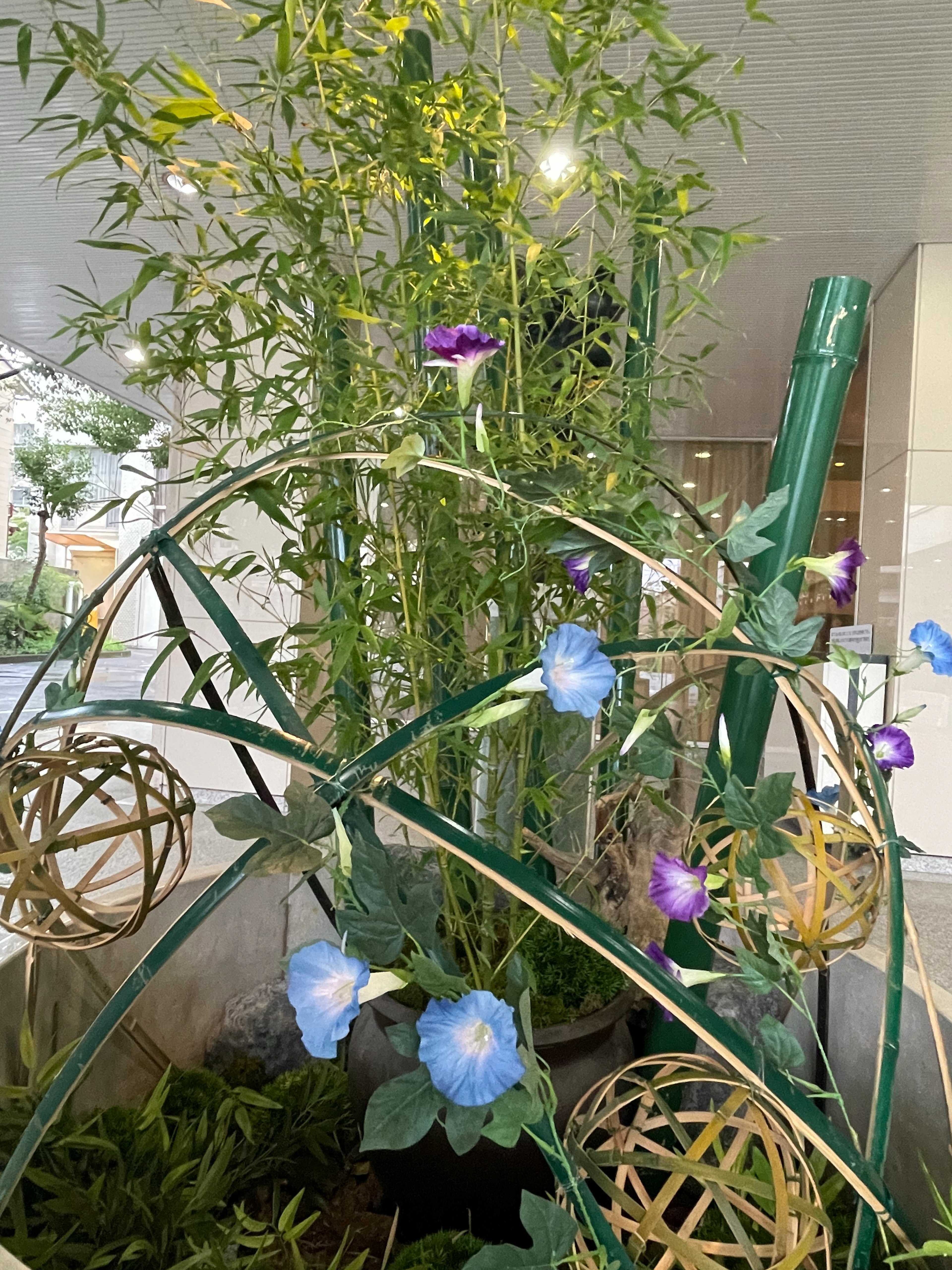 青い花と紫の花が咲く植物のアレンジメント竹の装飾と金色の球体が配置されている