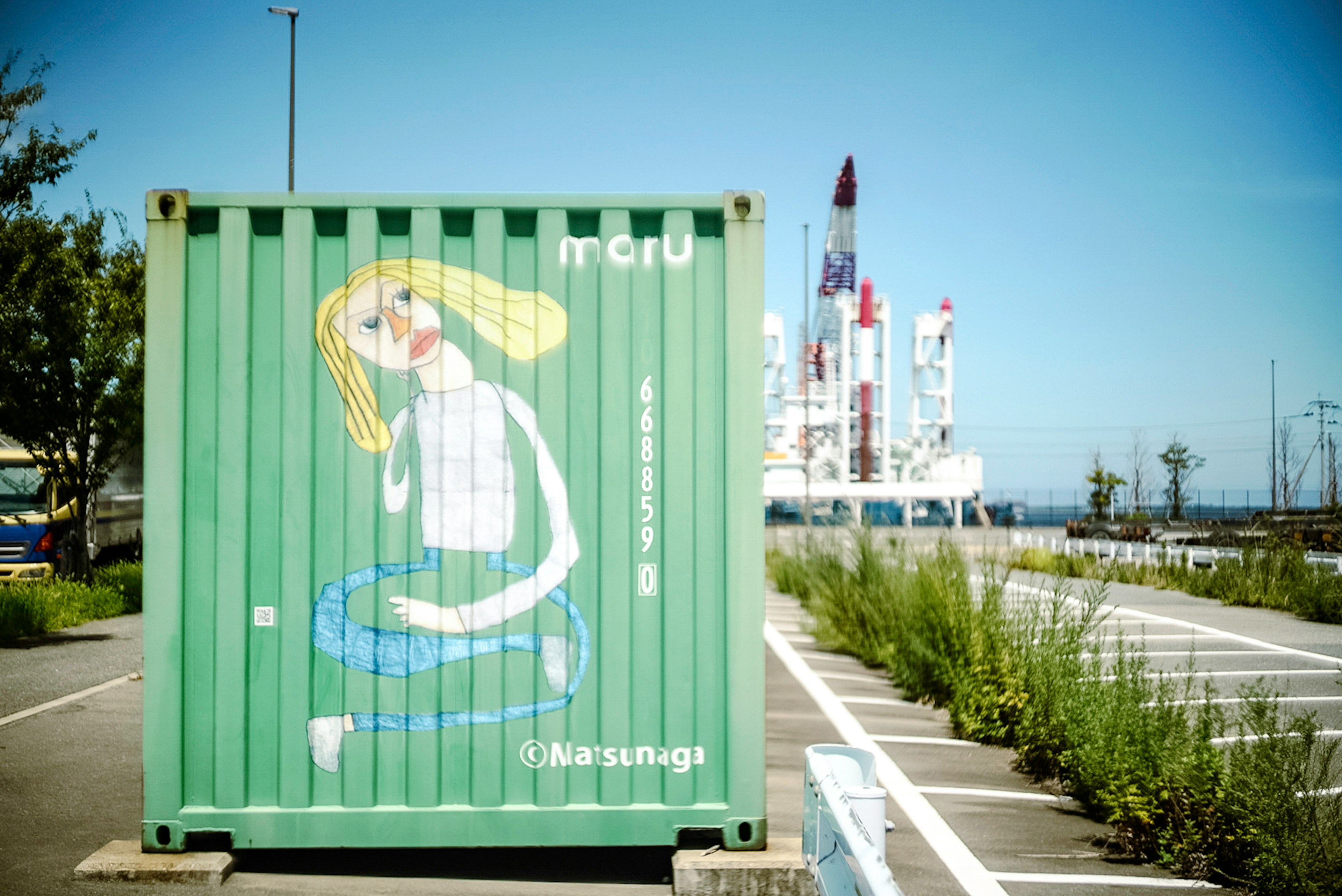 Grüner Container mit einer gemalten Illustration einer Frau und industriellen Strukturen im Hintergrund