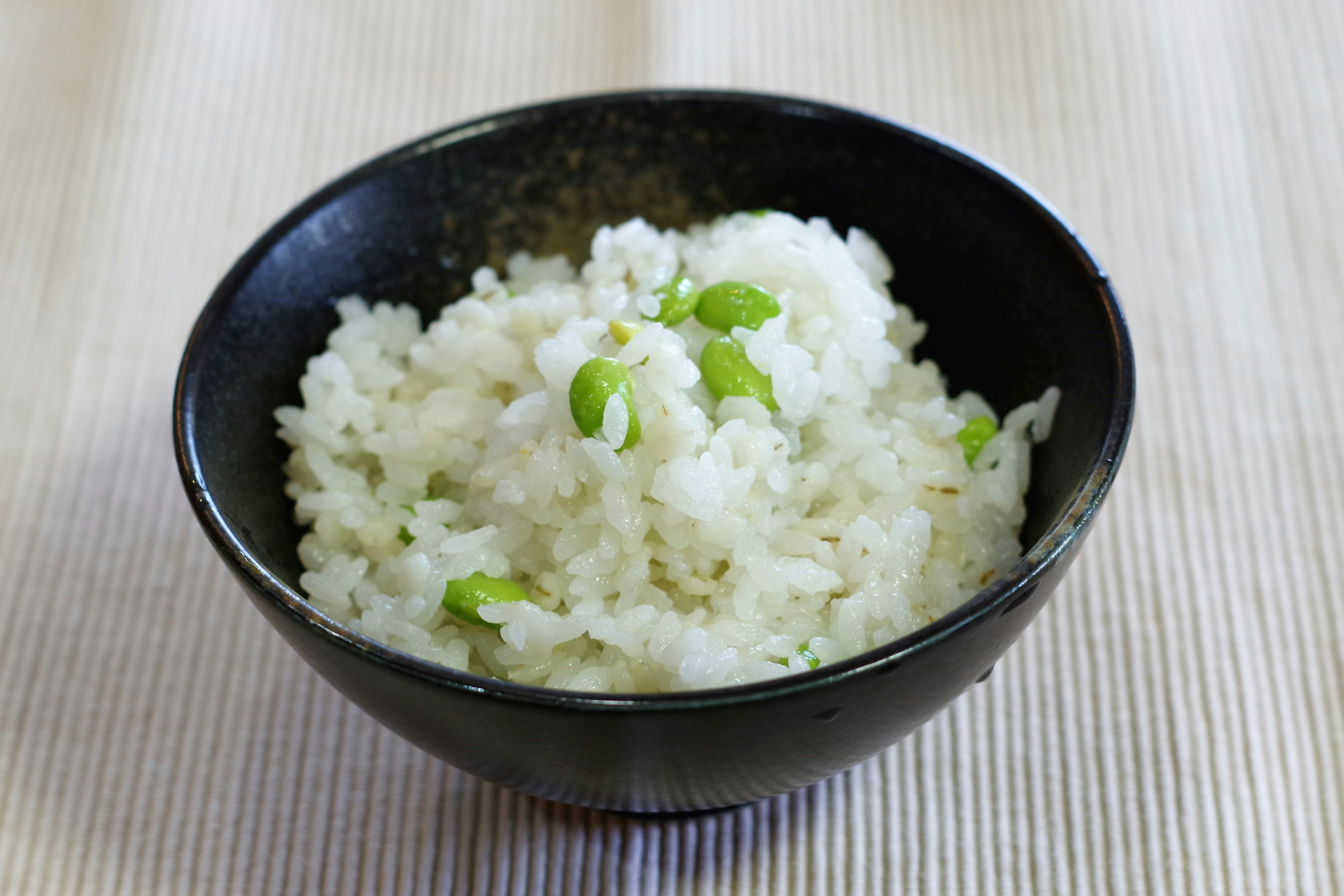 黒いボウルに盛られた白いご飯に緑の豆が散りばめられている