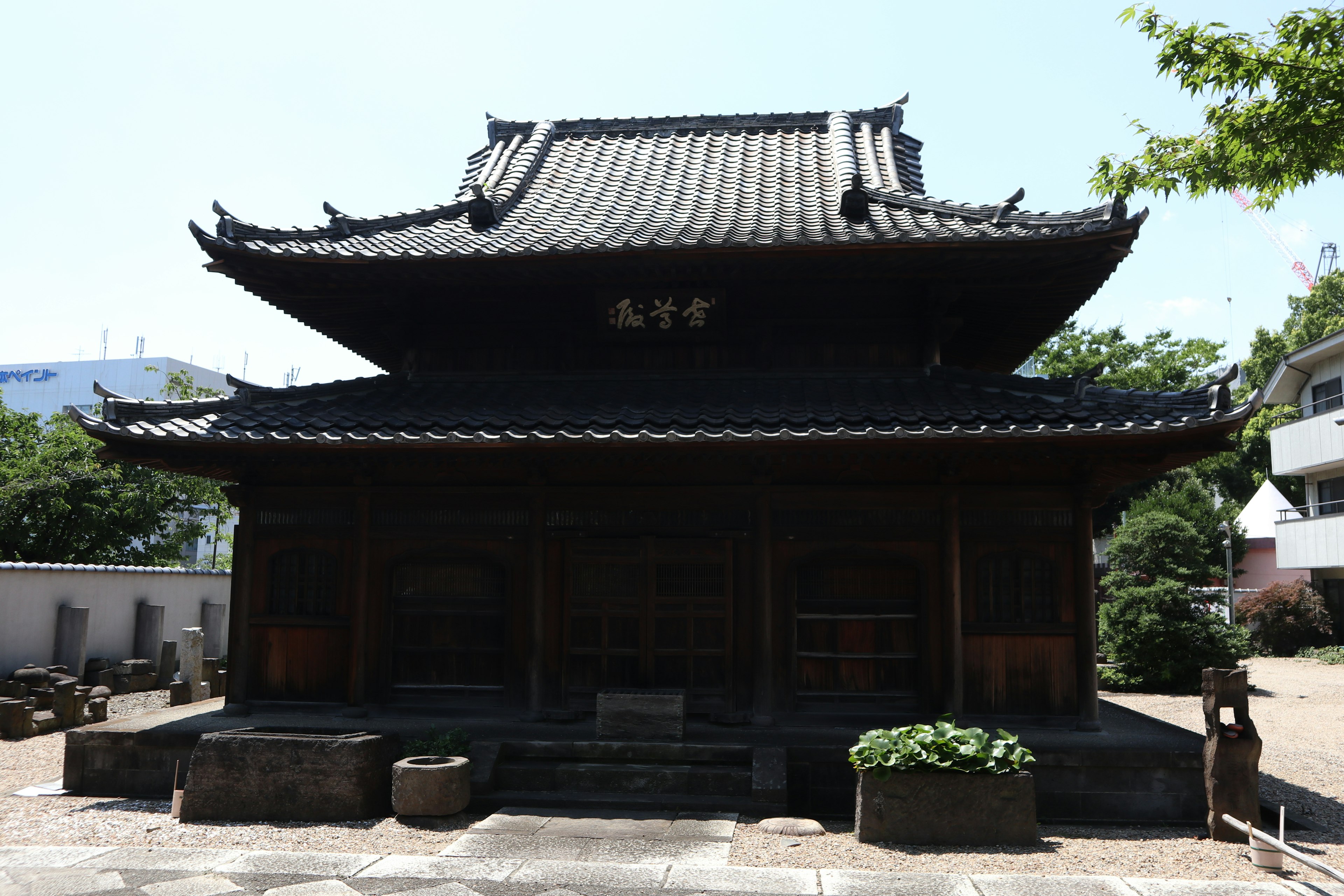 Exterior view of a traditional Japanese temple with distinctive roof design surrounded by greenery and modern buildings