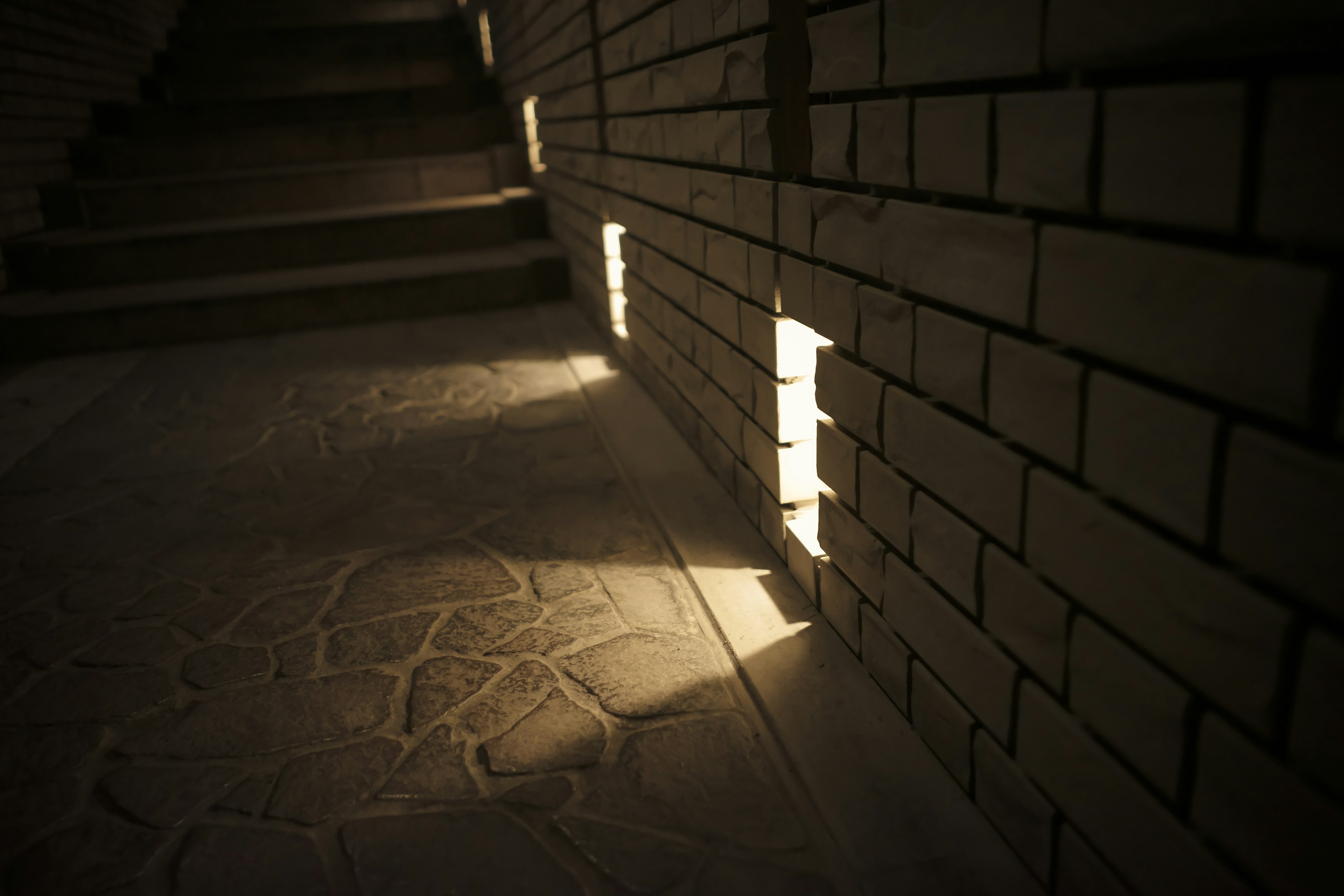 Brick wall near stairs with light shining through gaps