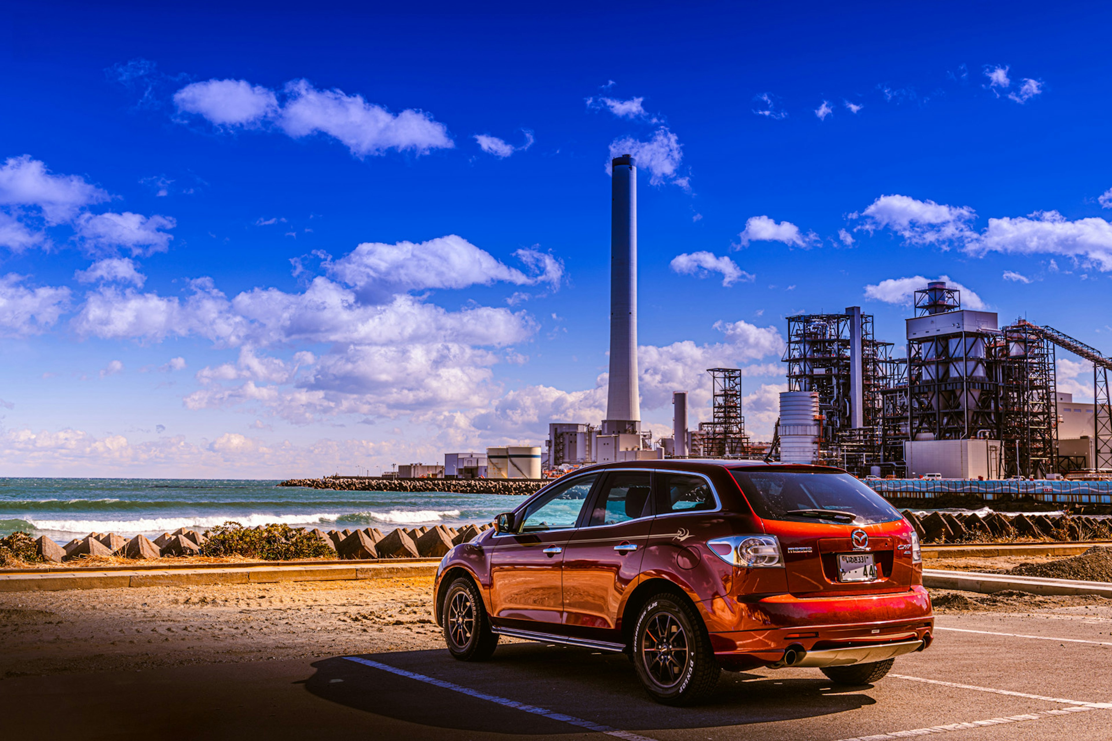 Orange car parked by the coast with a factory chimney in the background