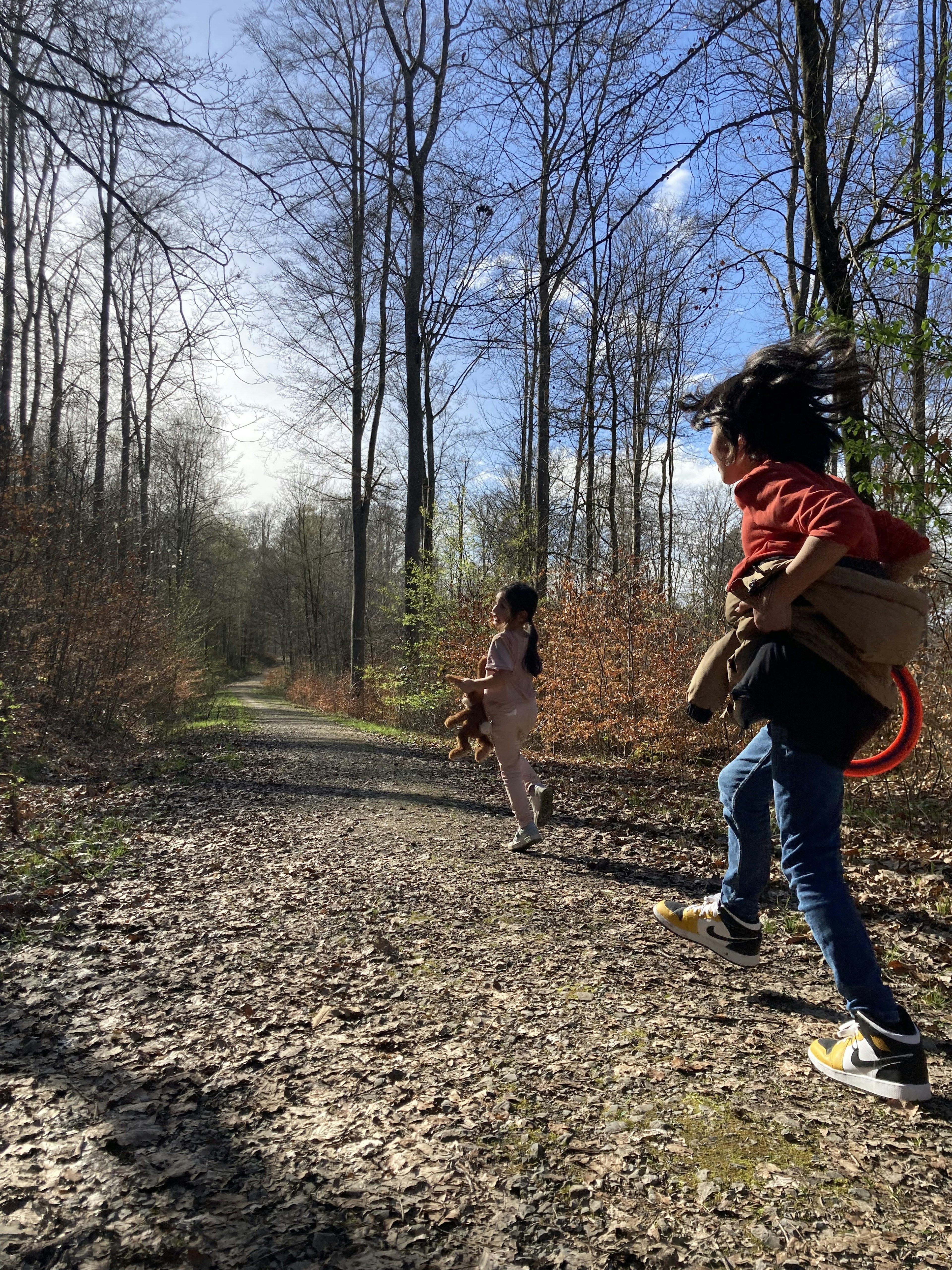 Two children running in a forest with a clear sky and trees in the background