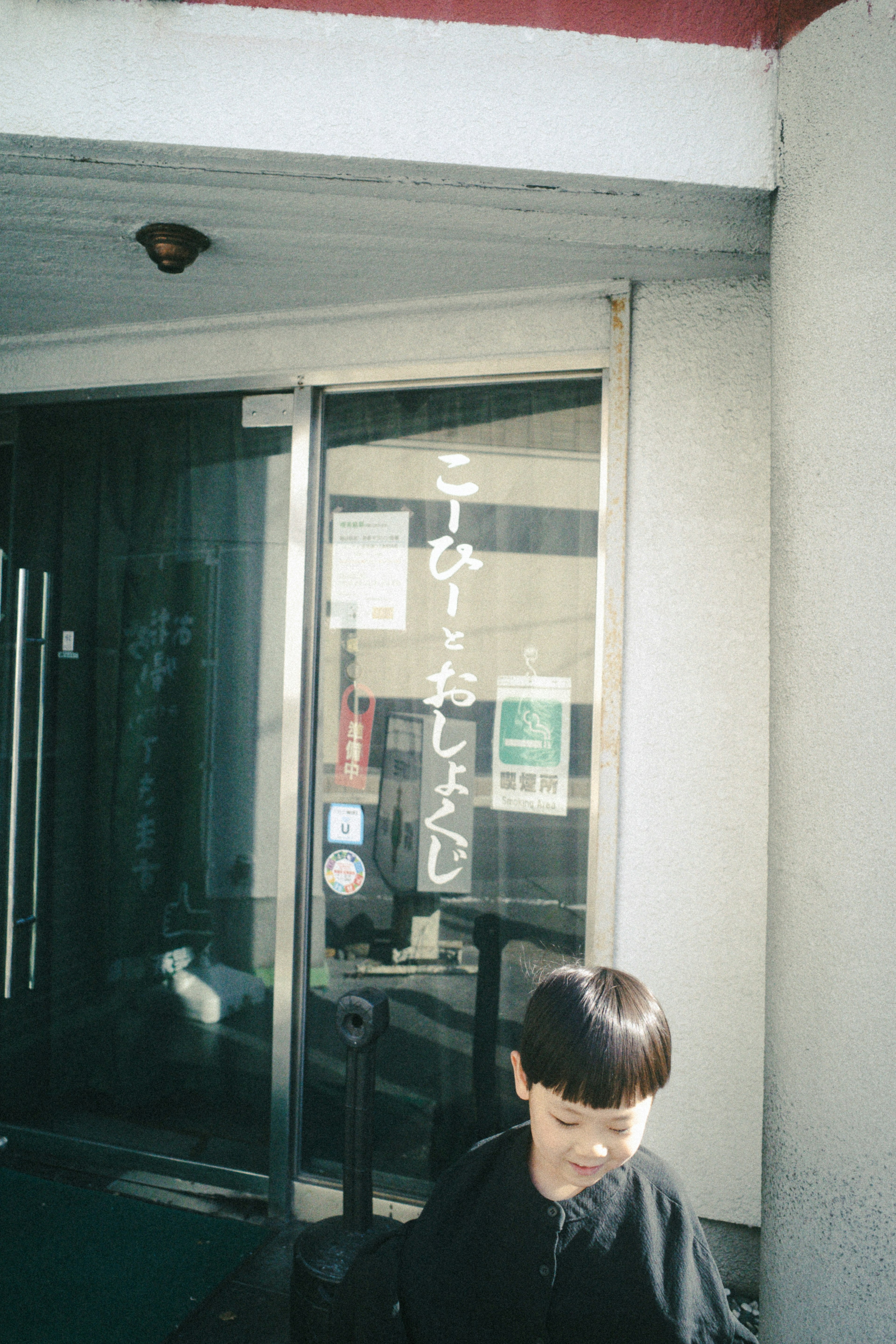 A child standing in front of a door with Japanese text visible on the glass