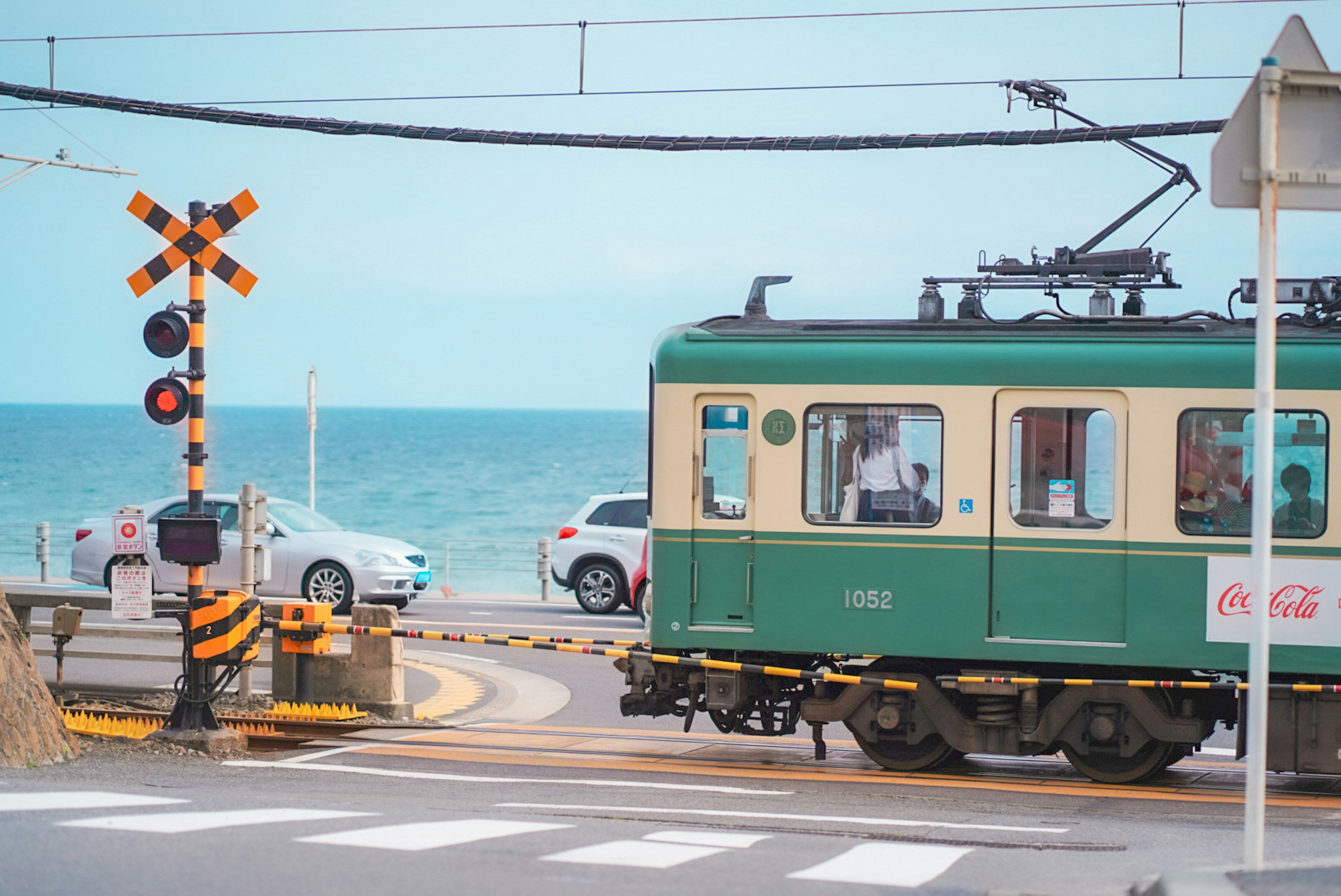 海の近くを走る緑色の電車と踏切の風景