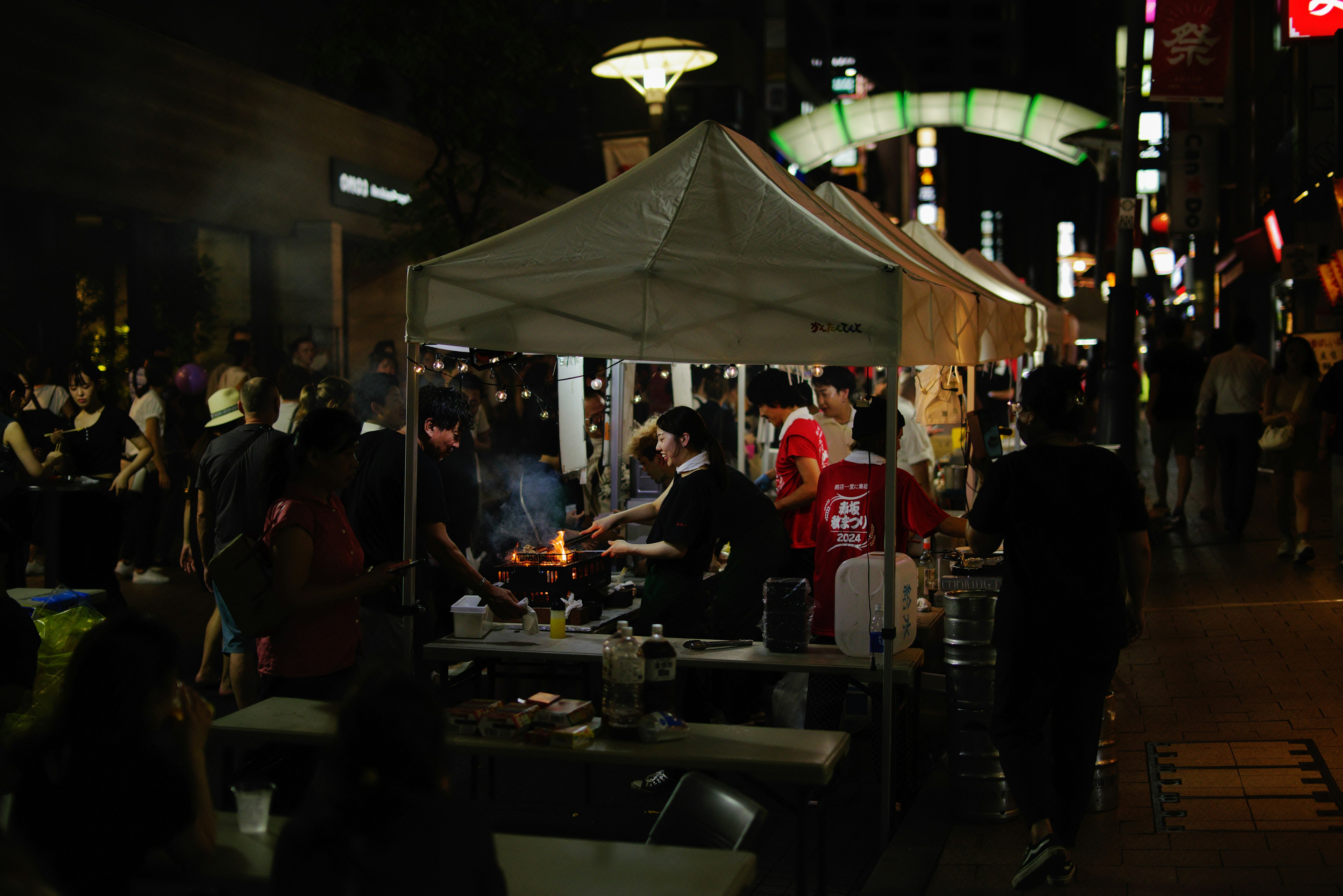 Scena di mercato notturno con persone che cucinano a un chiosco di cibo e una strada animata