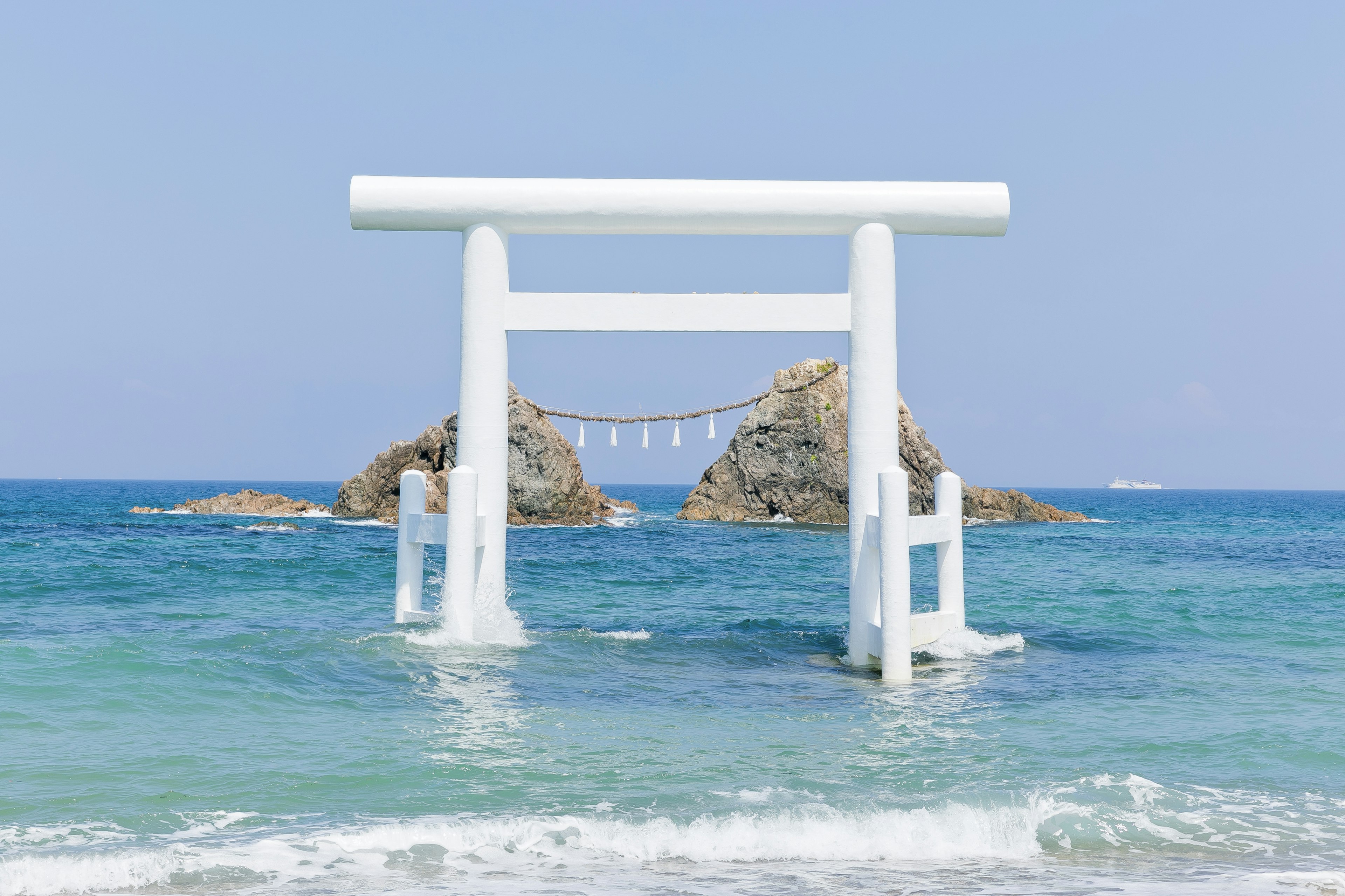 Portale torii bianco che si erge nell'oceano con rocce sullo sfondo